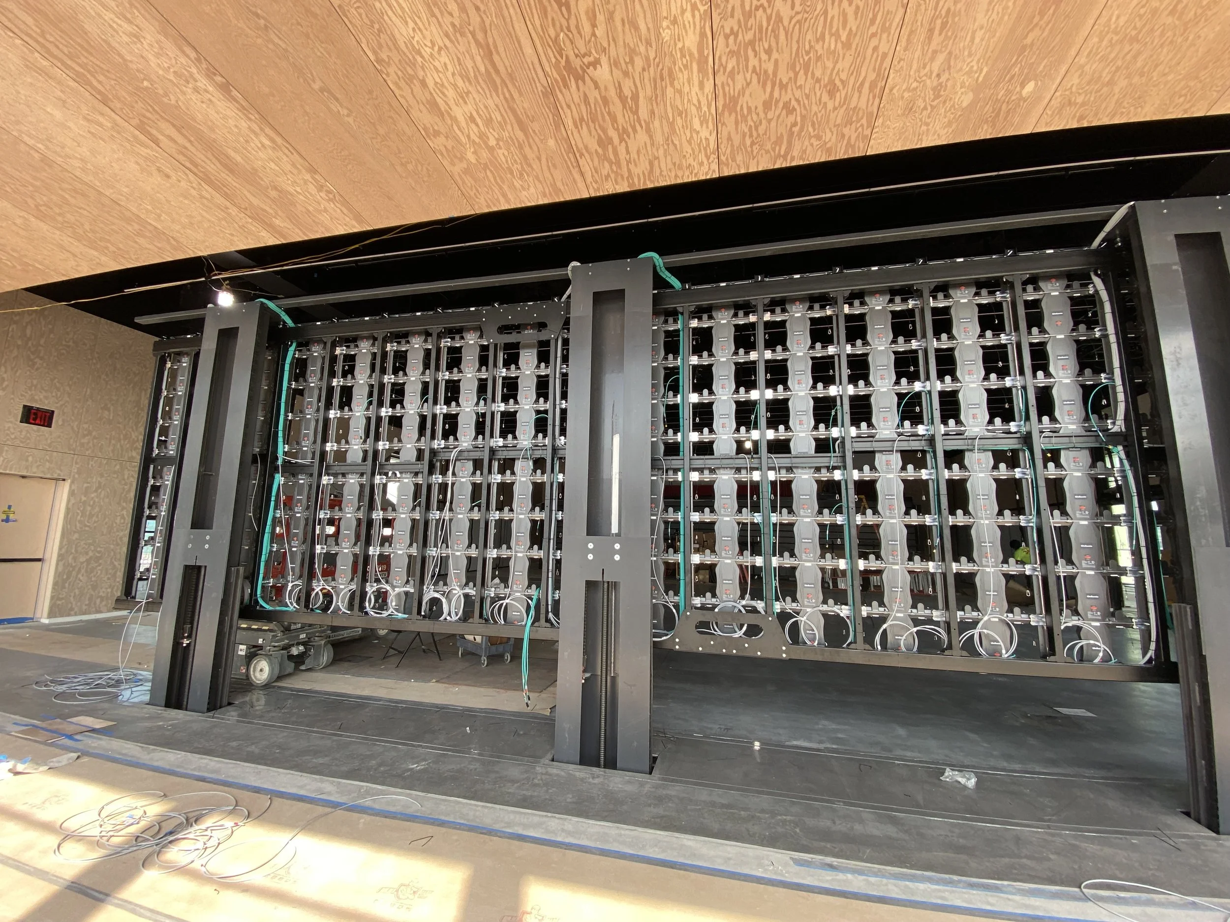 Large open room with a black metal frame structure, wires hanging, and equipment in the background.