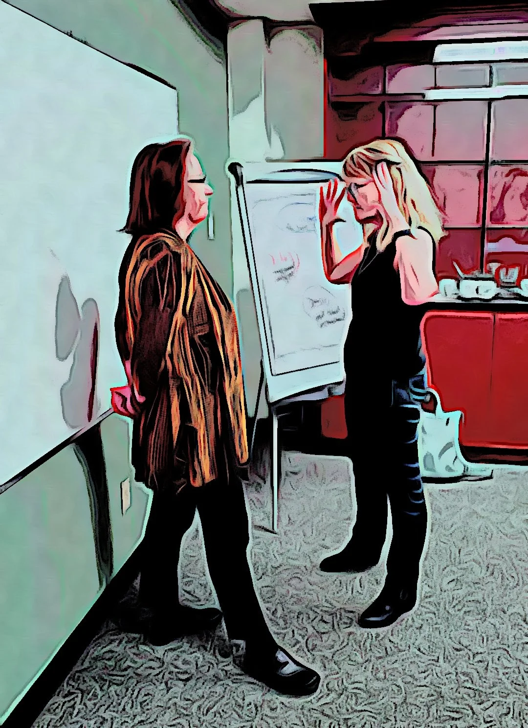 Two women standing and talking in a room with a whiteboard and kitchen in the background, one woman with blonde hair holding her head in her hand, the other with brown hair wearing glasses and a striped jacket.