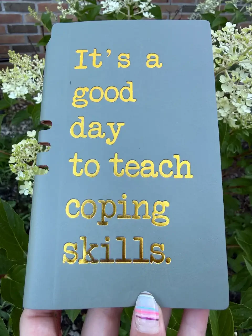 A blue notebook with yellow cut-out style letters that reads, 'It's a good day to teach coping skills,' help by Bree Ruoff LISW-S Ohio therapist offering online services for anxiety, school anxiety, empowerment,