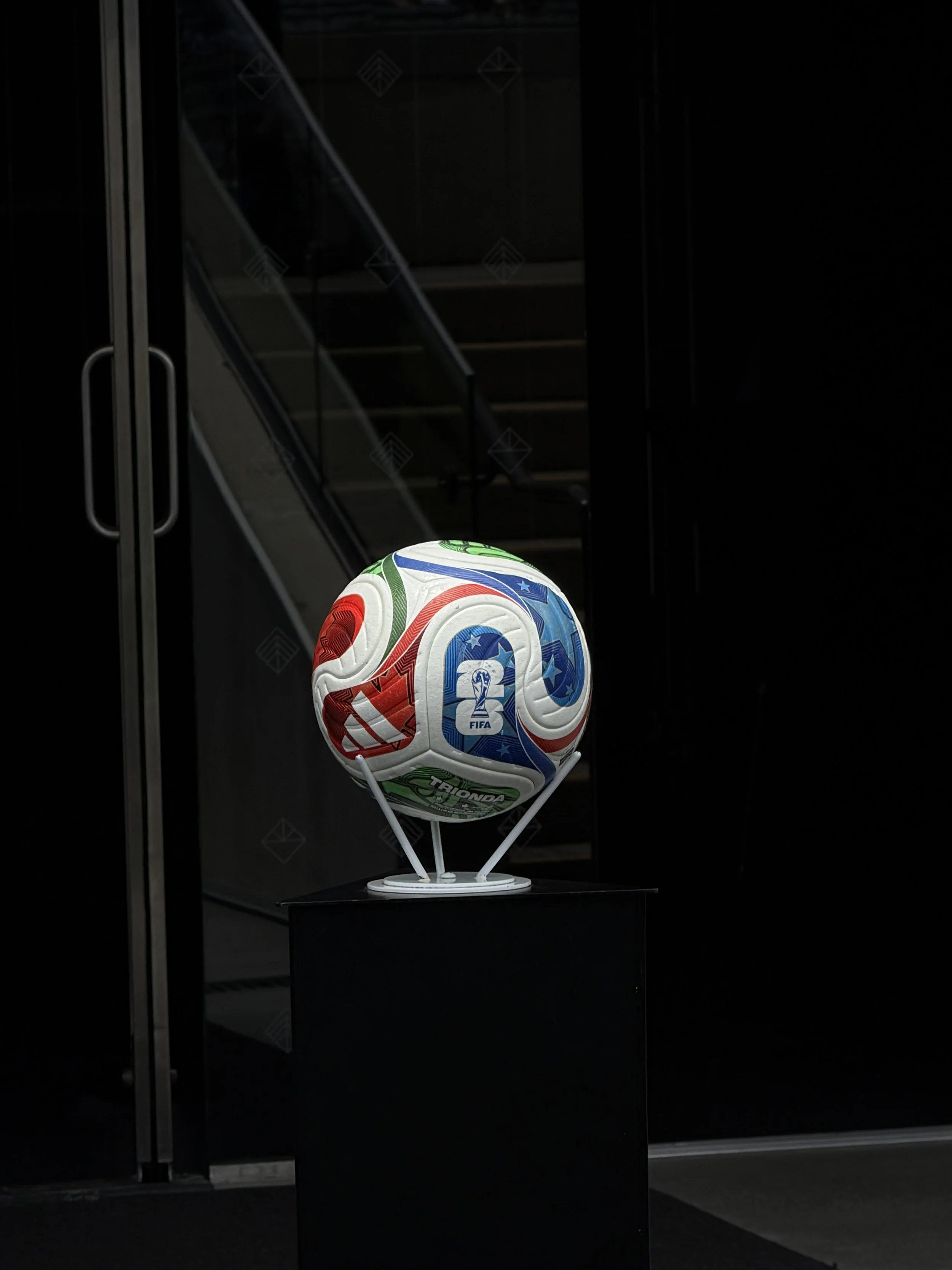 A colorful FIFA World Cup soccer ball on a stand, displayed in a dark exhibition space with a black background.