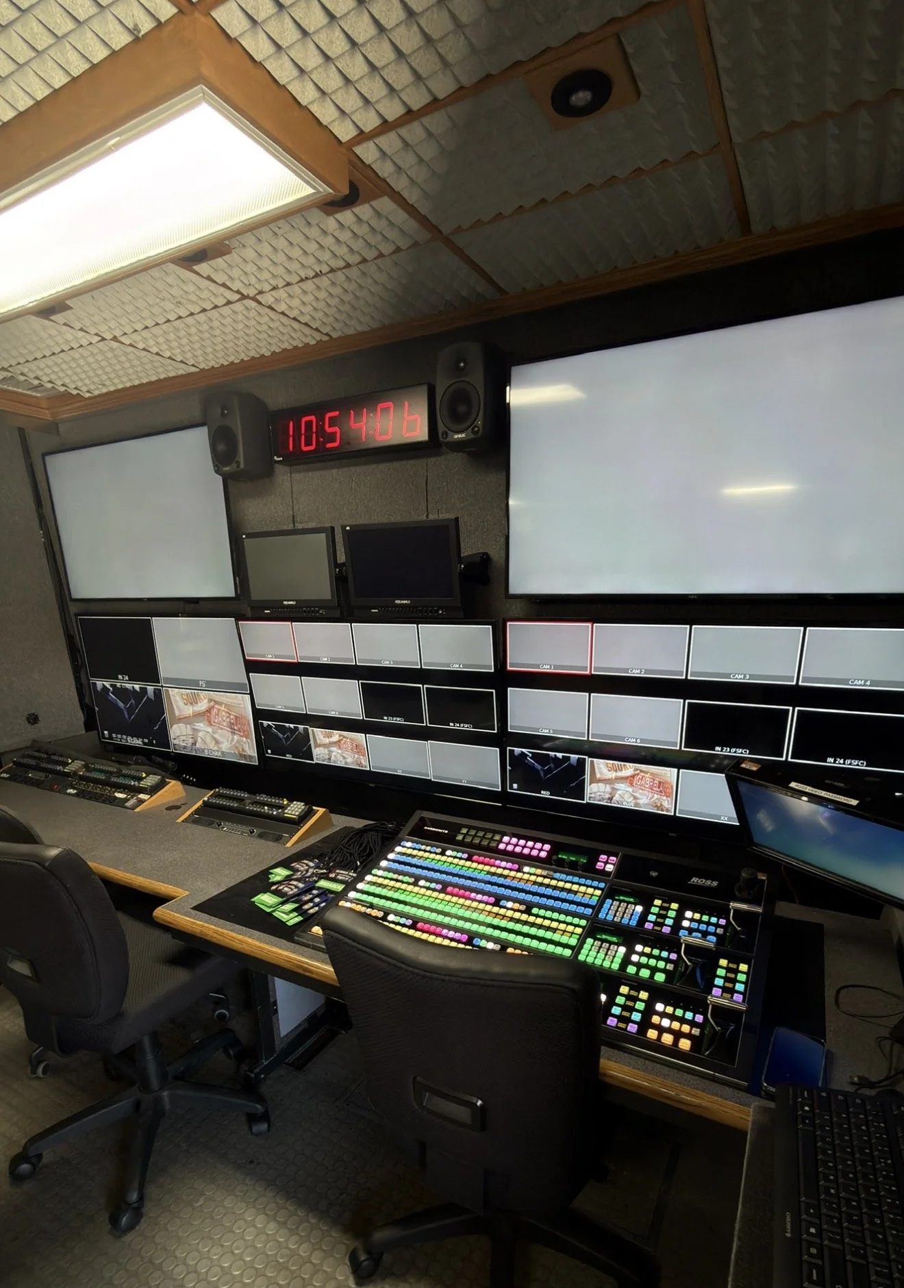 Television production control room with multiple monitors, sound equipment, colorful control board, and a digital clock showing 10:54:06.