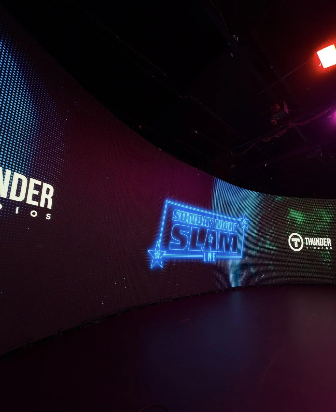 Neon sign displaying 'Sunday Night Slam Live' with stars, part of a larger digital display in a dark room.
