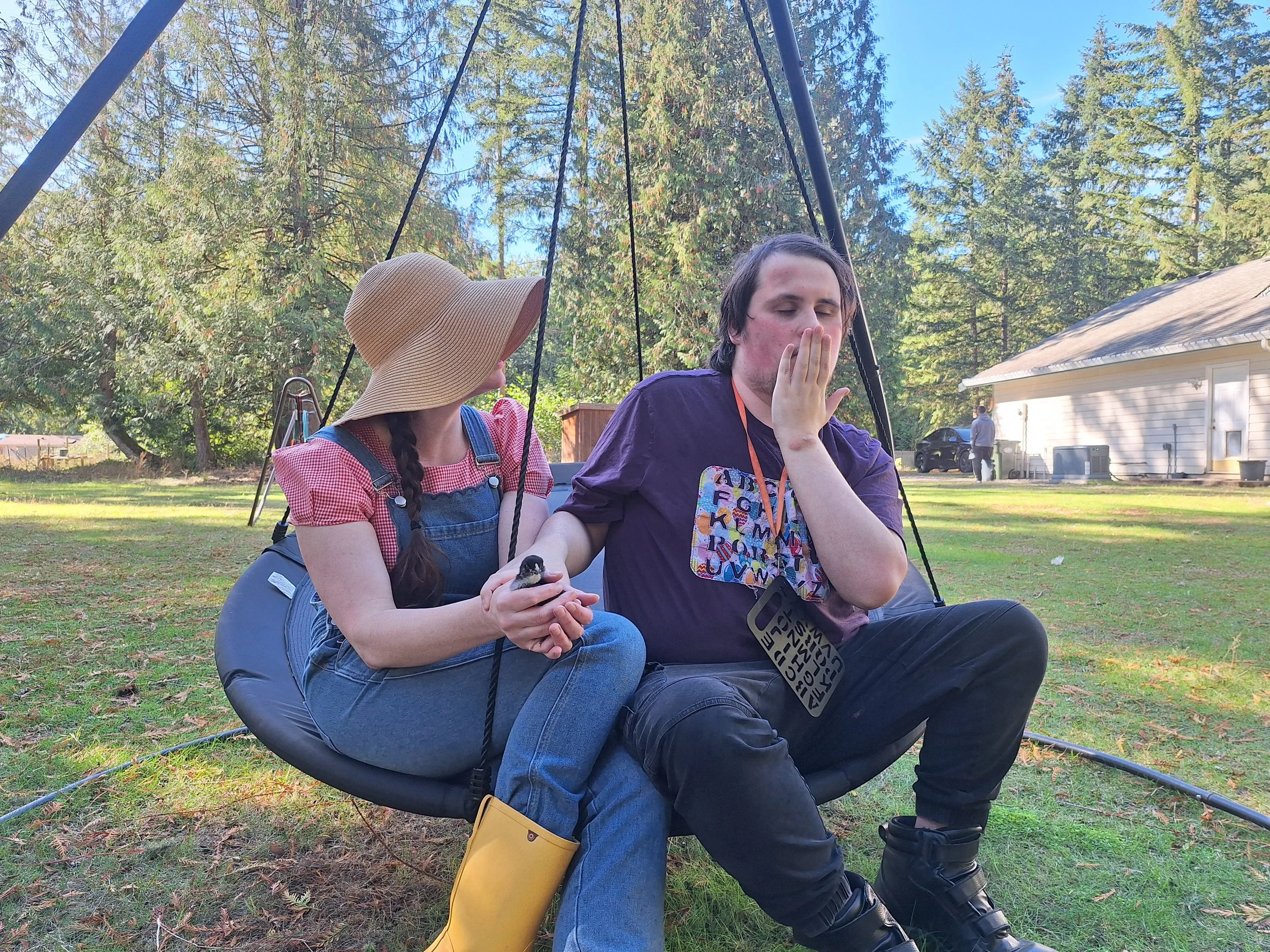 A participant and staff member sitting on an outdoor circle swing with a small chick.