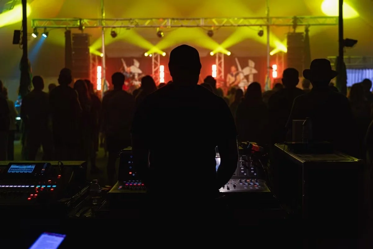 Silhouette d'un technicien de son face à un public lors d'un concert ou festival, avec des lumières de scène colorées.