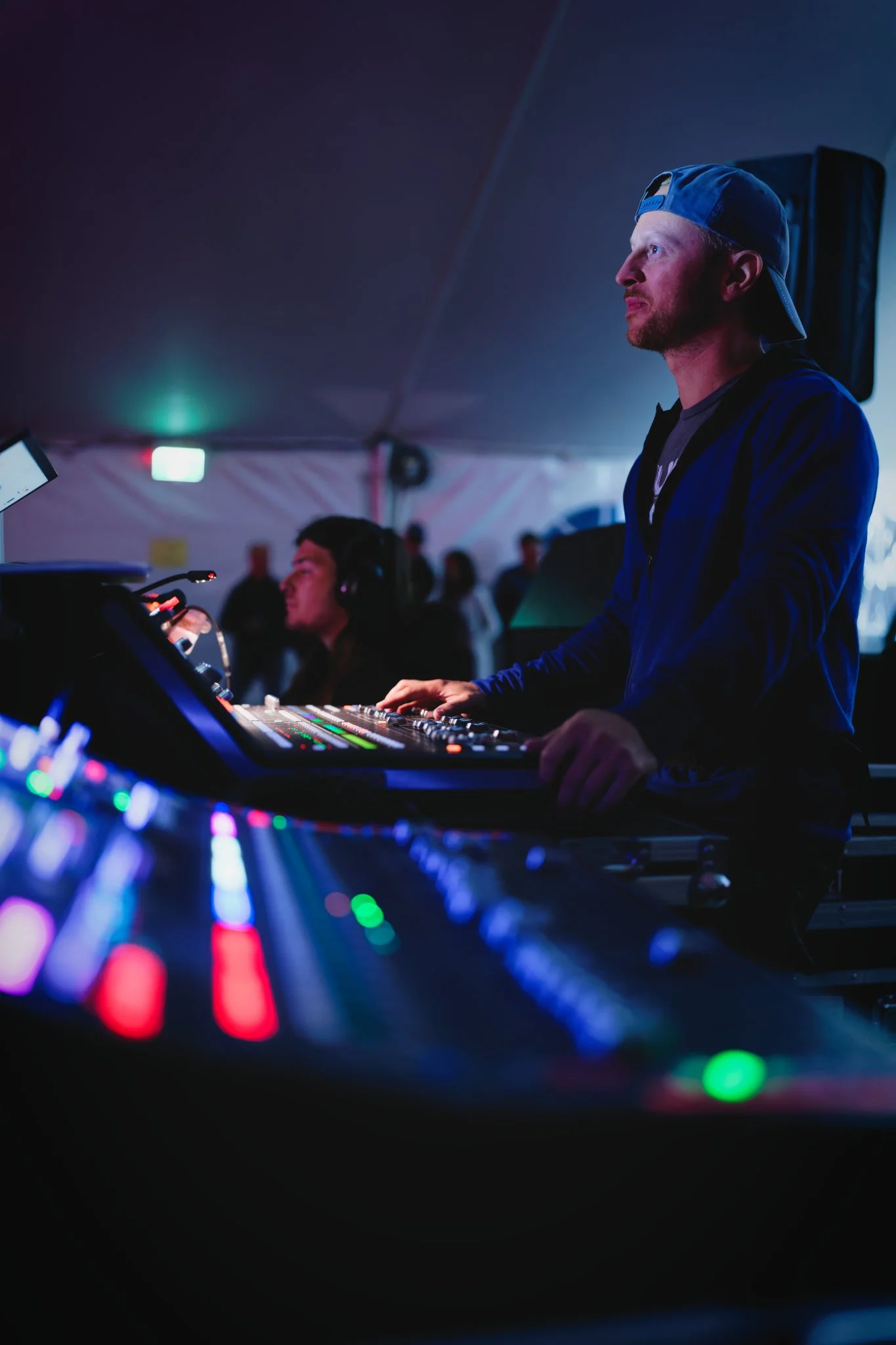 Un technicien de son lors d'un événement, avec des équipements de mixage lumineux et des personnes en arrière-plan.