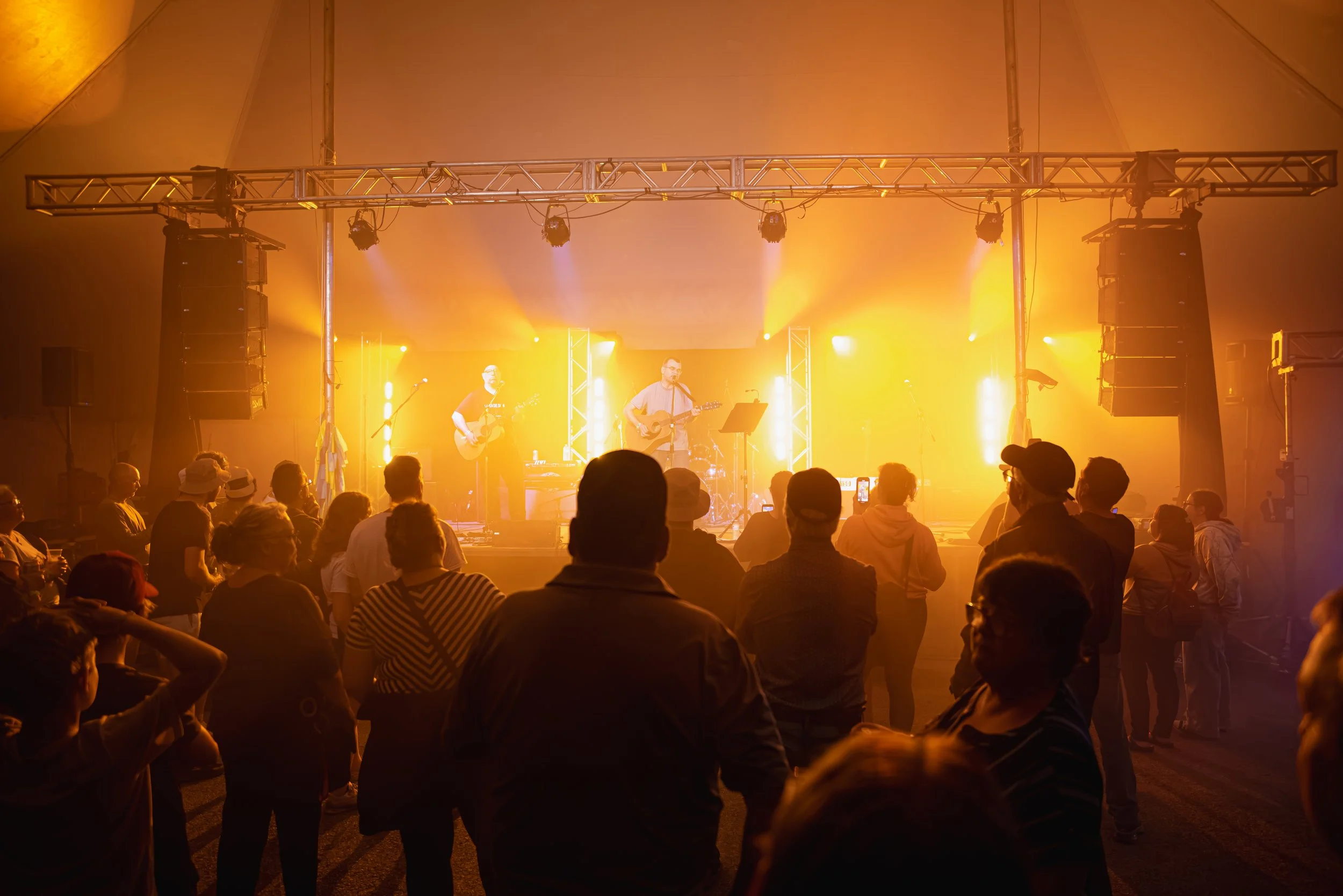 Concert avec deux musiciens jouant de la guitare sur scène, entourés de lumières jaunes et une foule regardant.