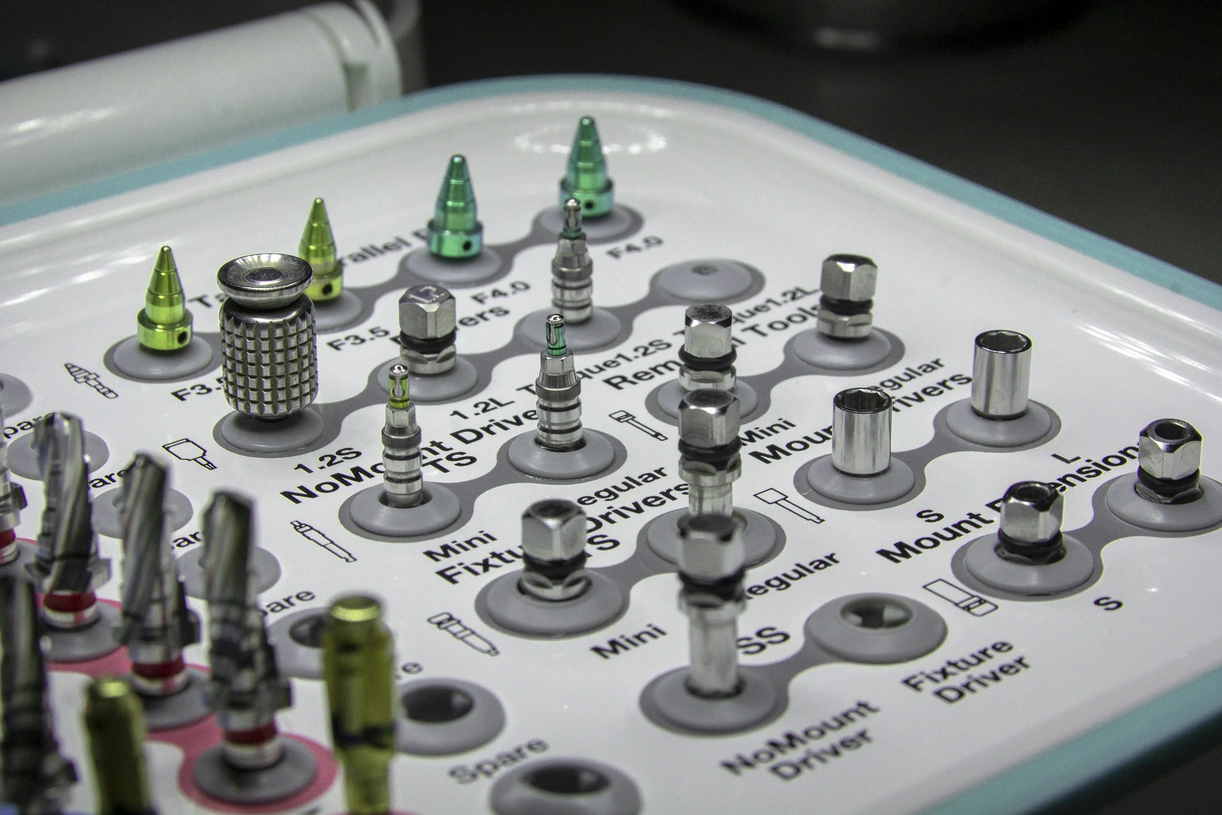 Close-up of a medical or dental instrument kit with various small metal and plastic components arranged on a board, including tips, screws, and mounts.