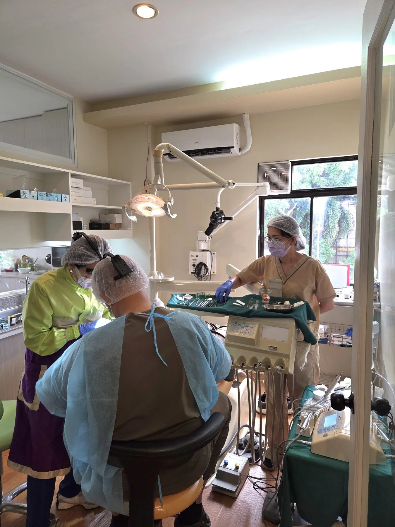 Medical team performing surgery in a well-lit operating room, with doctors and nurses in scrubs, masks, and hair covers, surrounding a patient on the operating table.