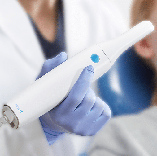 A healthcare professional holding a medical device with a blue button, wearing blue gloves, in a clinical setting.