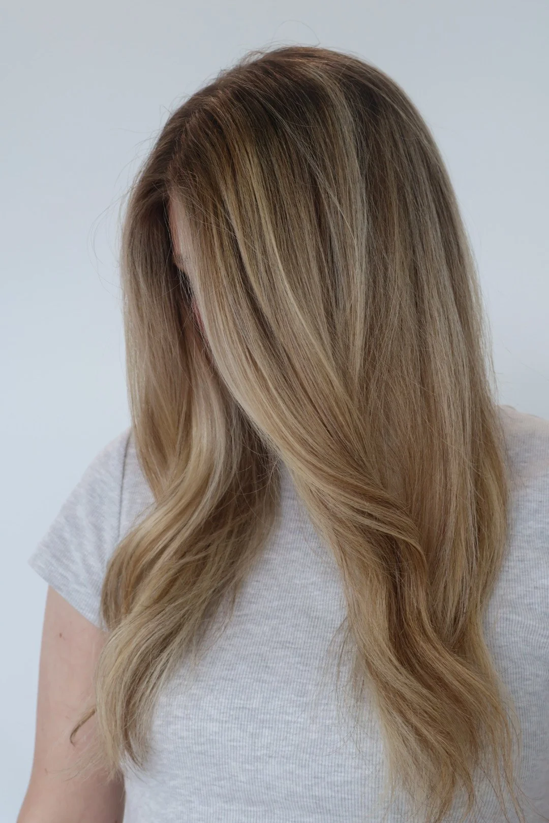 A woman with long, wavy blonde hair wearing a white t-shirt against a plain light background.