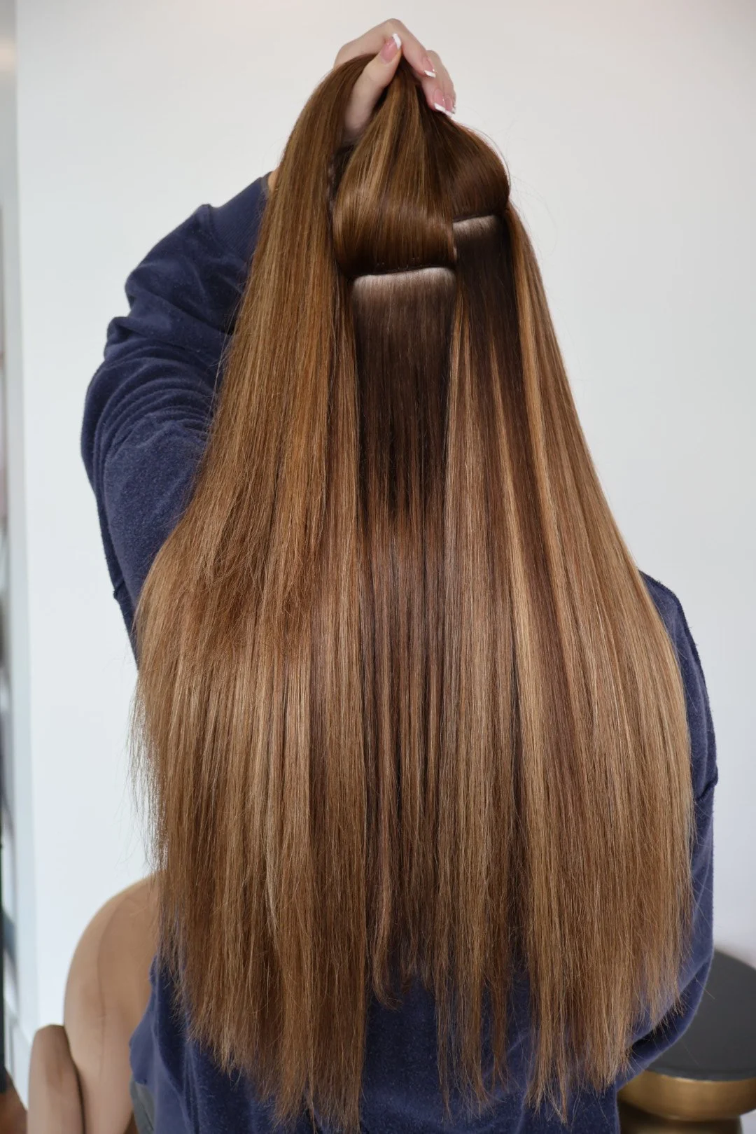 Person holding Harper Ellis hair extensions with long, straight, brown hair with a section pinned up, wearing a dark sweatshirt.