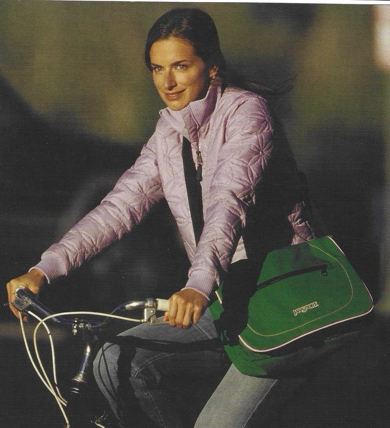 A woman riding a bicycle wearing a light purple jacket, with a green backpack.