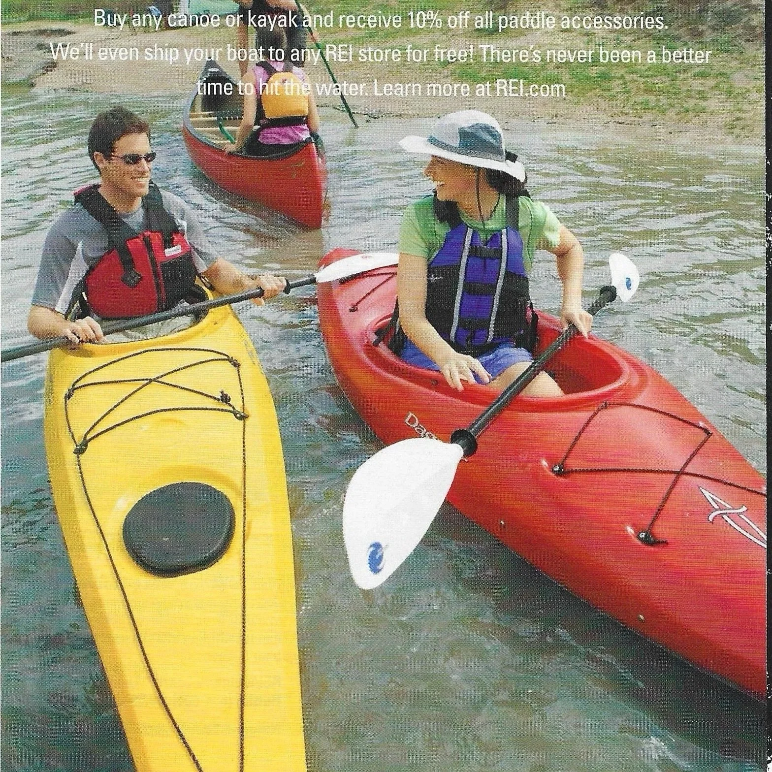 Two people in kayaks on a lake with a person in a yellow kayak and a person in a red kayak, both wearing life jackets and hats, engaging in conversation.