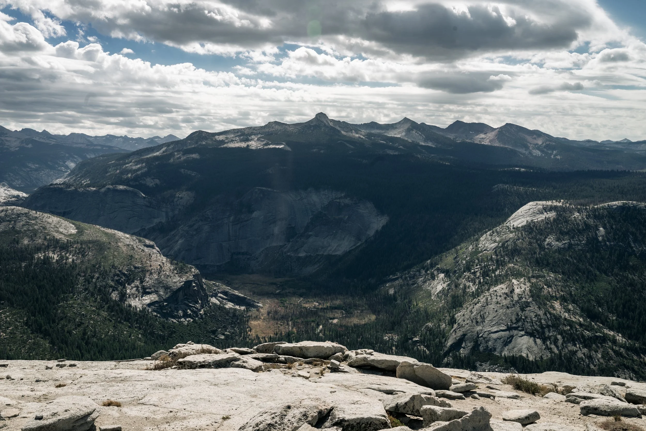 Scenic view of a mountain range with rugged peaks, forested slopes, and a cloudy sky overhead.