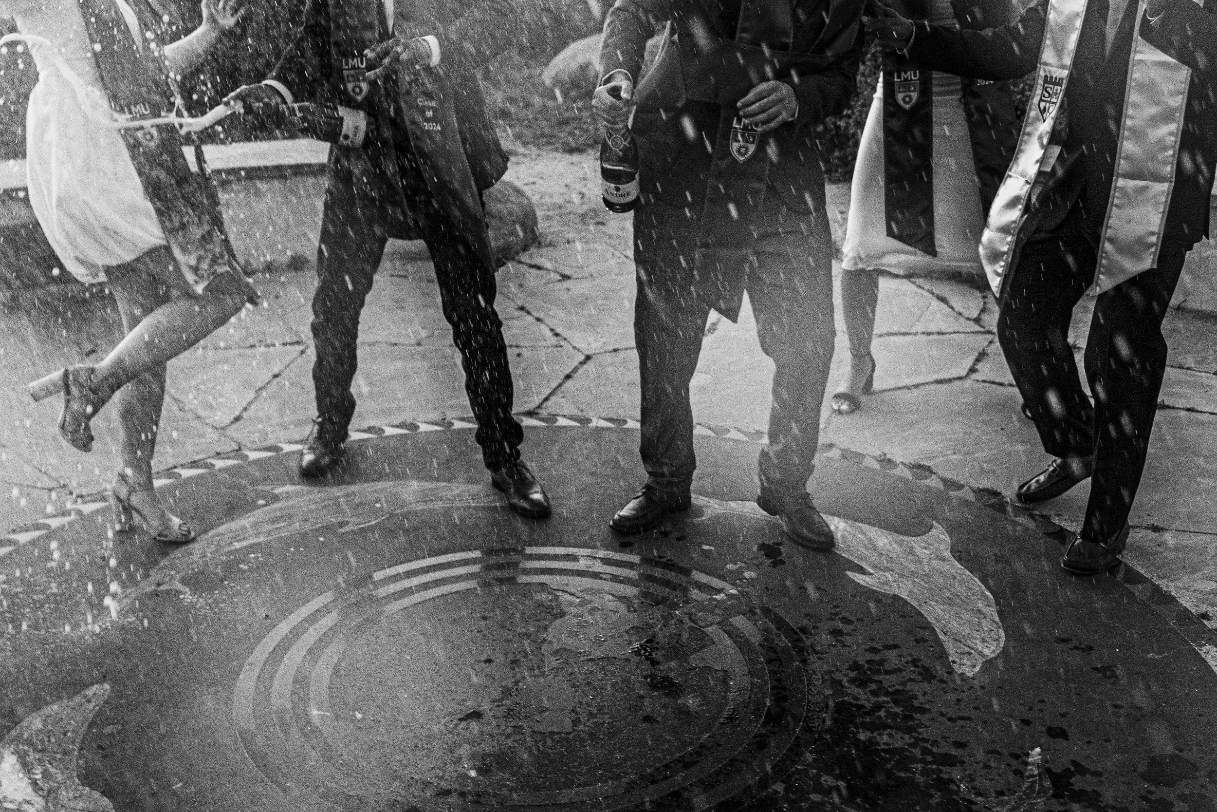 People standing and talking near a manhole cover in the rain, with water splashing around.