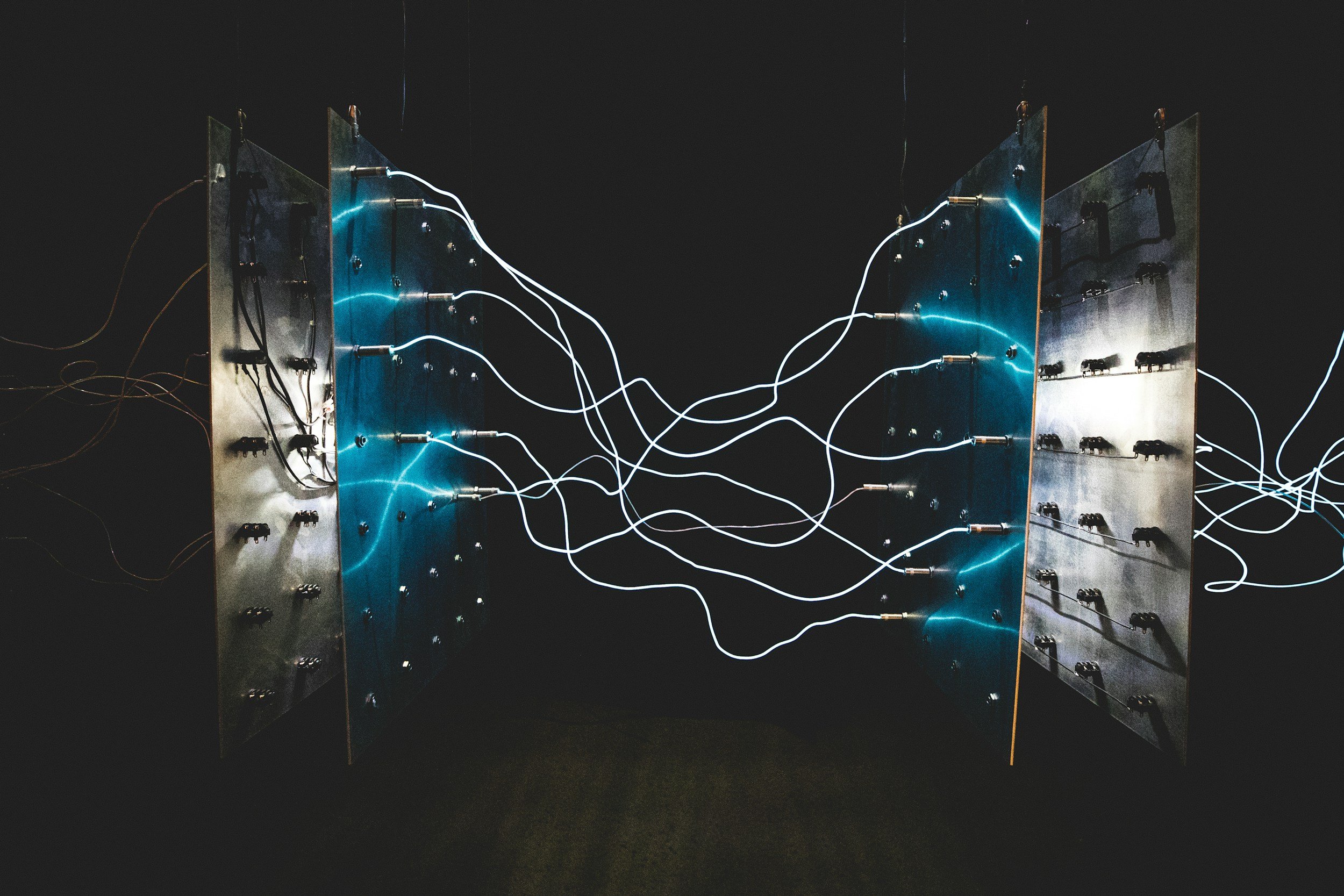 Two metallic panels with electrical wires and glowing blue electric arcs connecting their sides against a dark background.