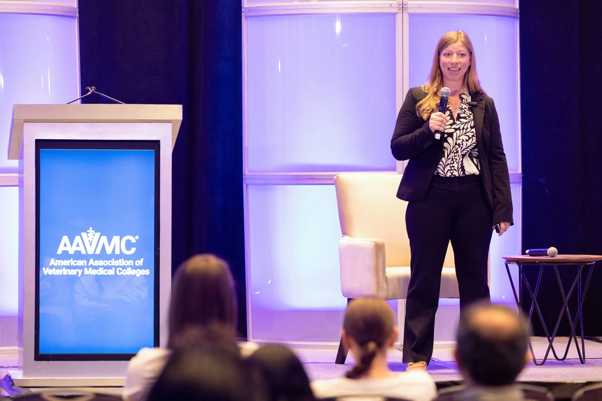 Dr. Michelle Schack on stage at a conference. There is a large screen with the American Association of Veterinary Medical Colleges logo and a podium to her left.