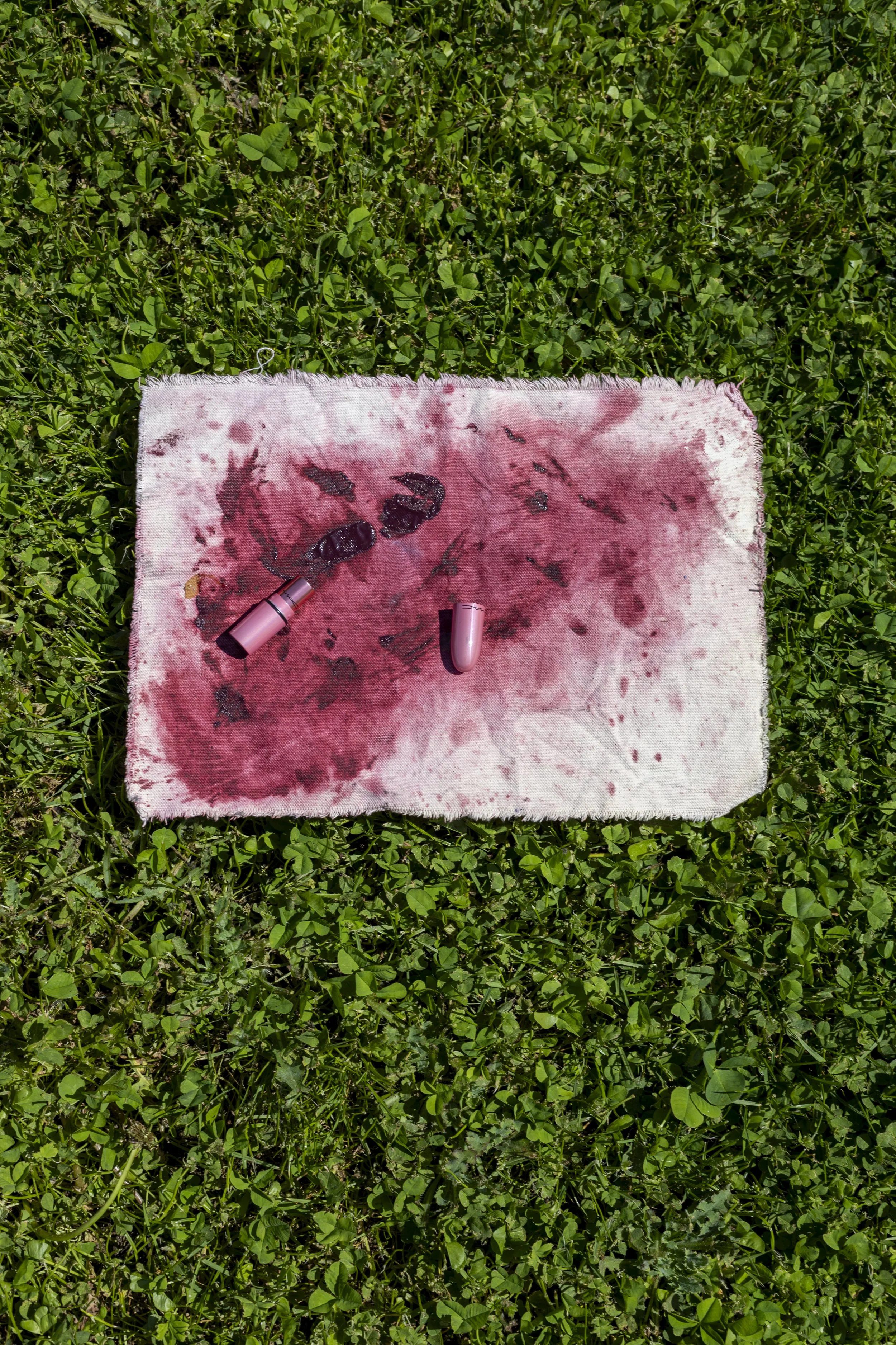 A blood-stained towel with two lipstick tubes and blood smears, lying on green grass.