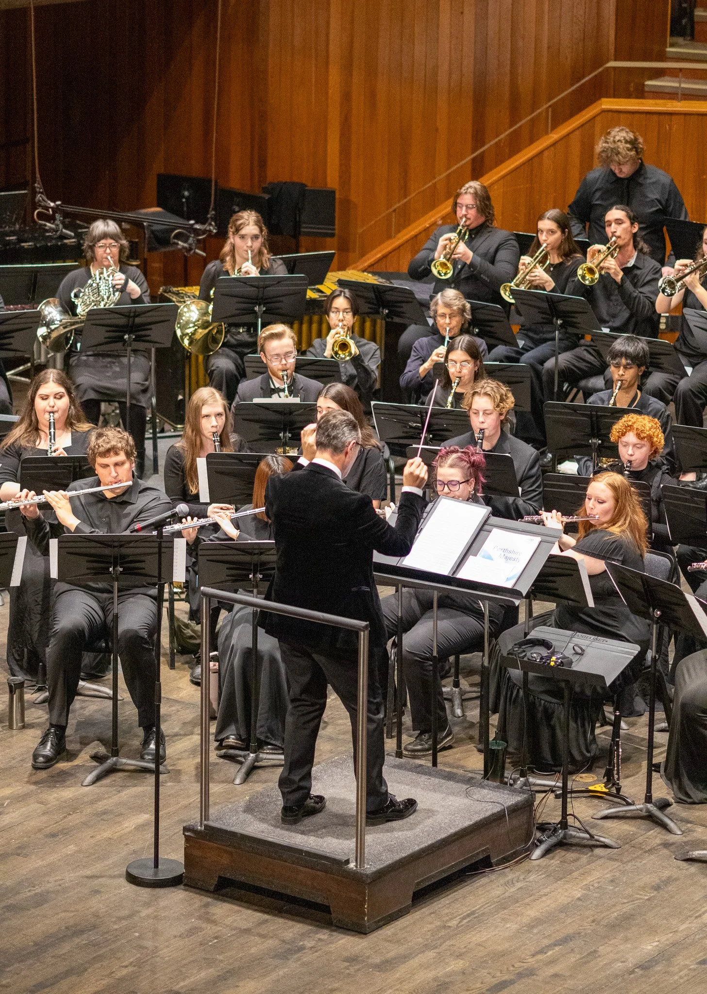 An orchestra performing on stage with musicians playing various instruments, led by a conductor standing on a podium.