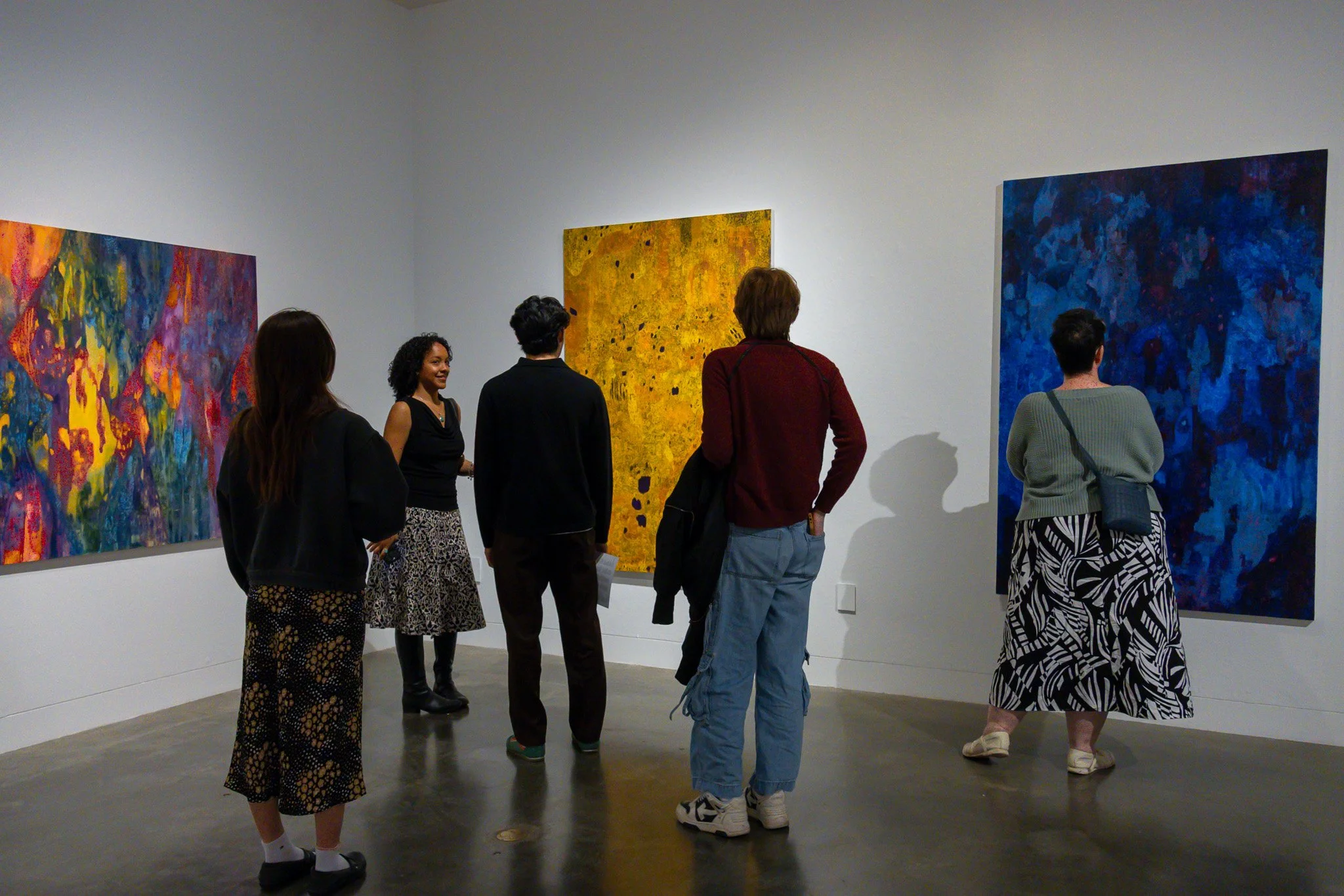People viewing colorful abstract paintings in an art gallery