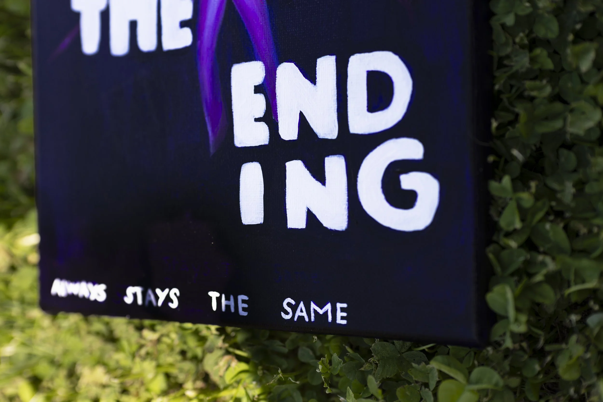 Close-up of a chalkboard sign with the words 'THE END' and some text below, placed outdoors among green shrubbery.