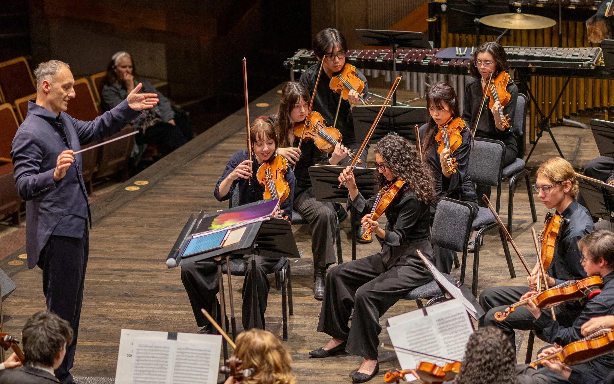 Orchestra conductor leading young musicians playing string instruments during a concert.