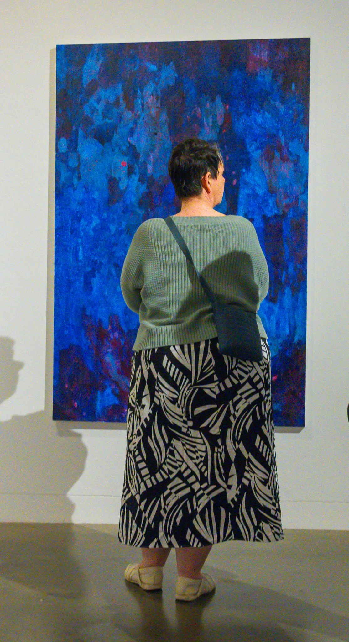 Person standing in front of blue abstract painting in an art gallery.