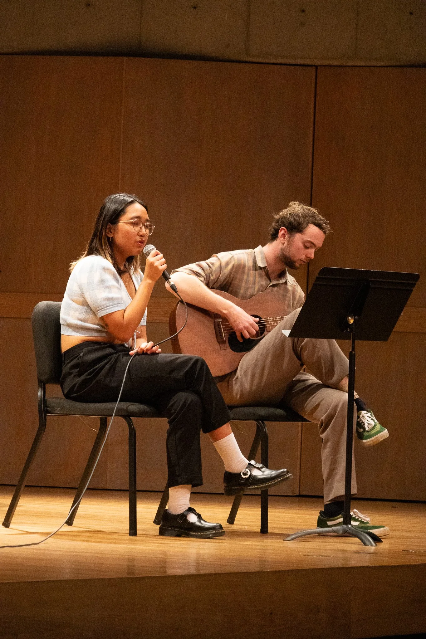 A woman singing into a microphone and a man playing an acoustic guitar on stage during a performance.