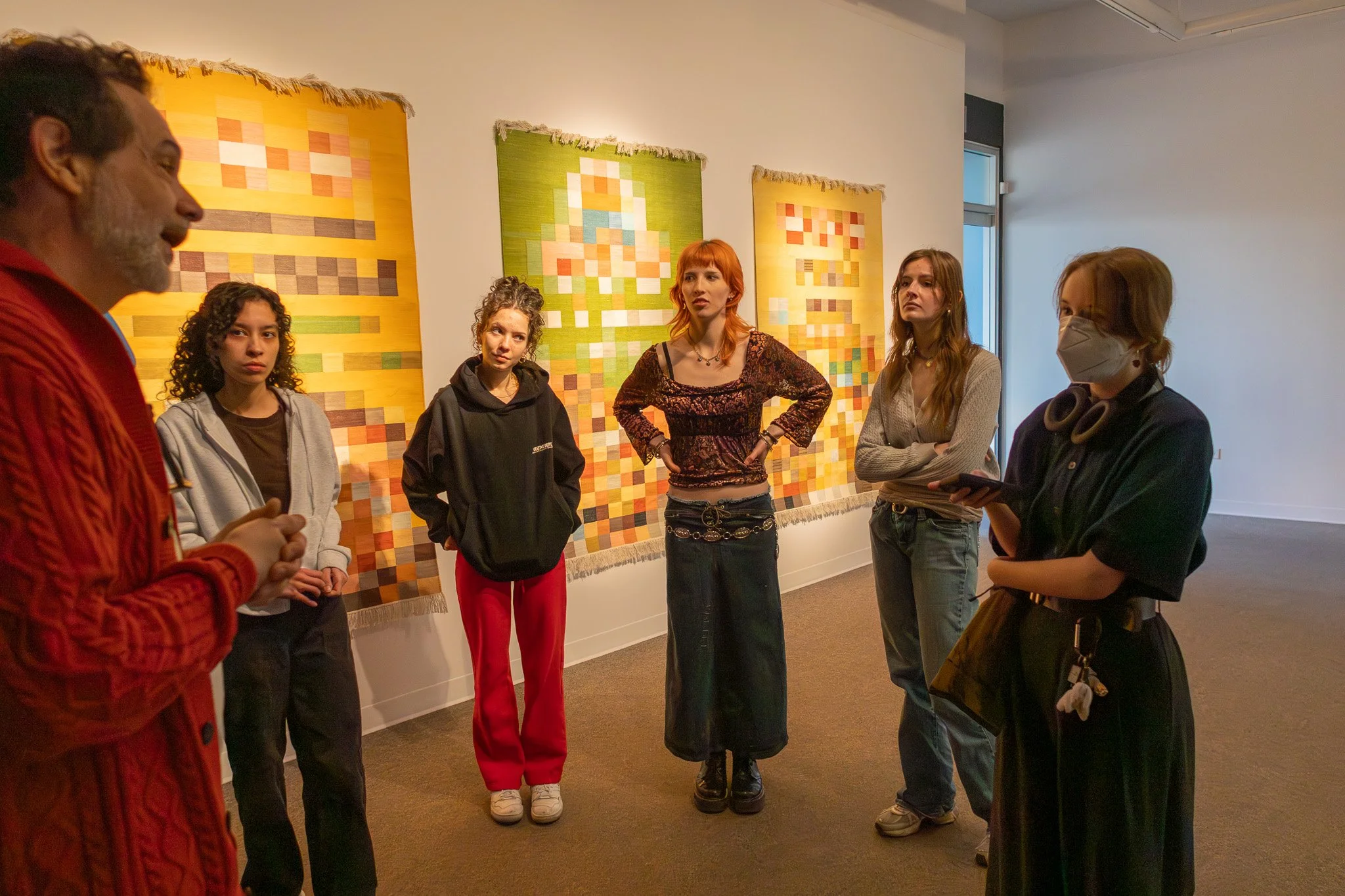 Group of six people standing and having a conversation in an art gallery with quilted wall hangings in the background.