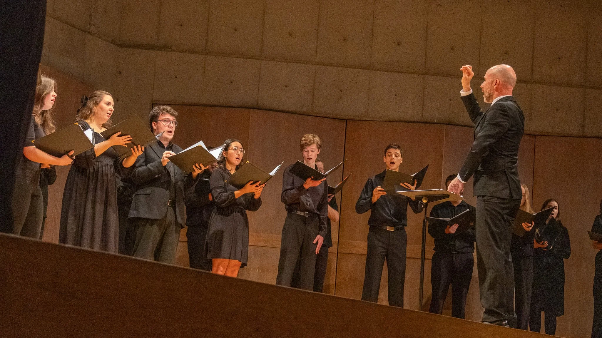 A choir of young people singing under the direction of a conductor in a concert hall.