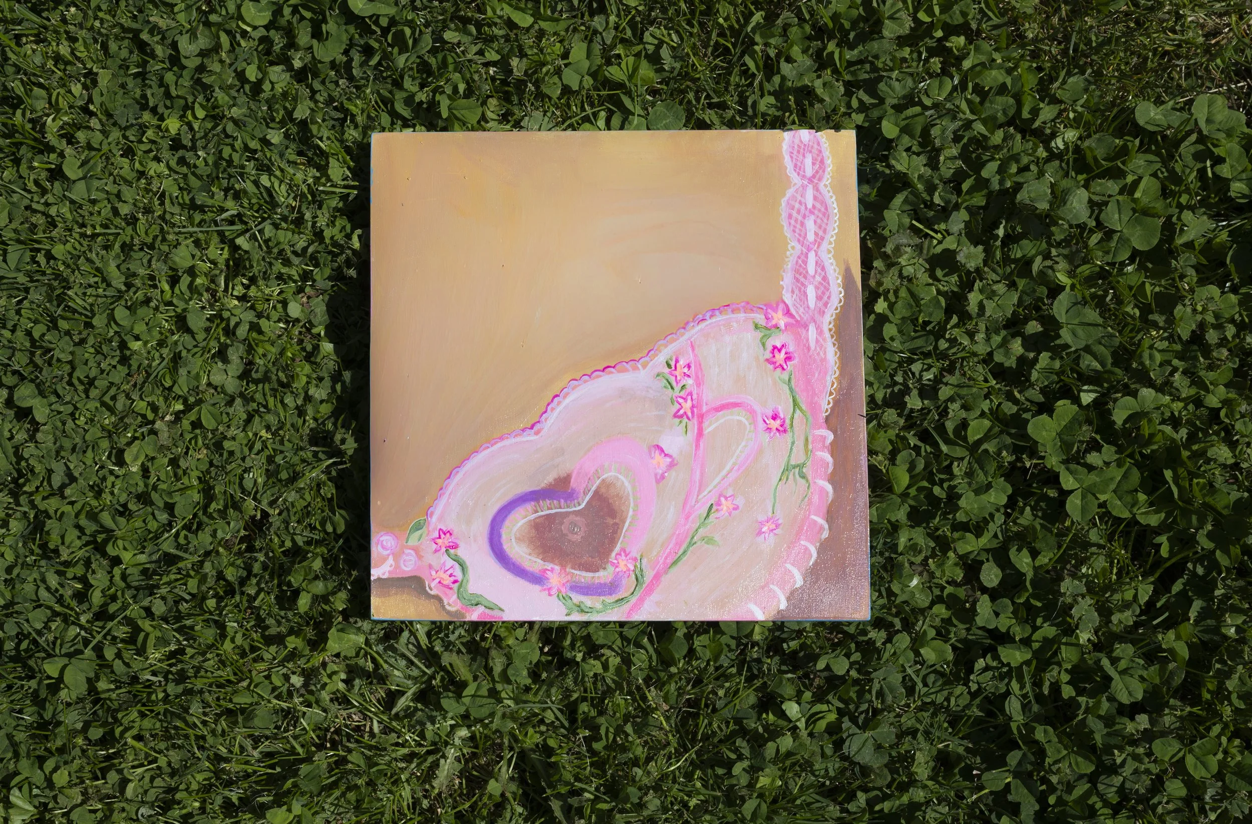A painting with pink and purple hearts, flowers, and swirling designs, placed on green grass.