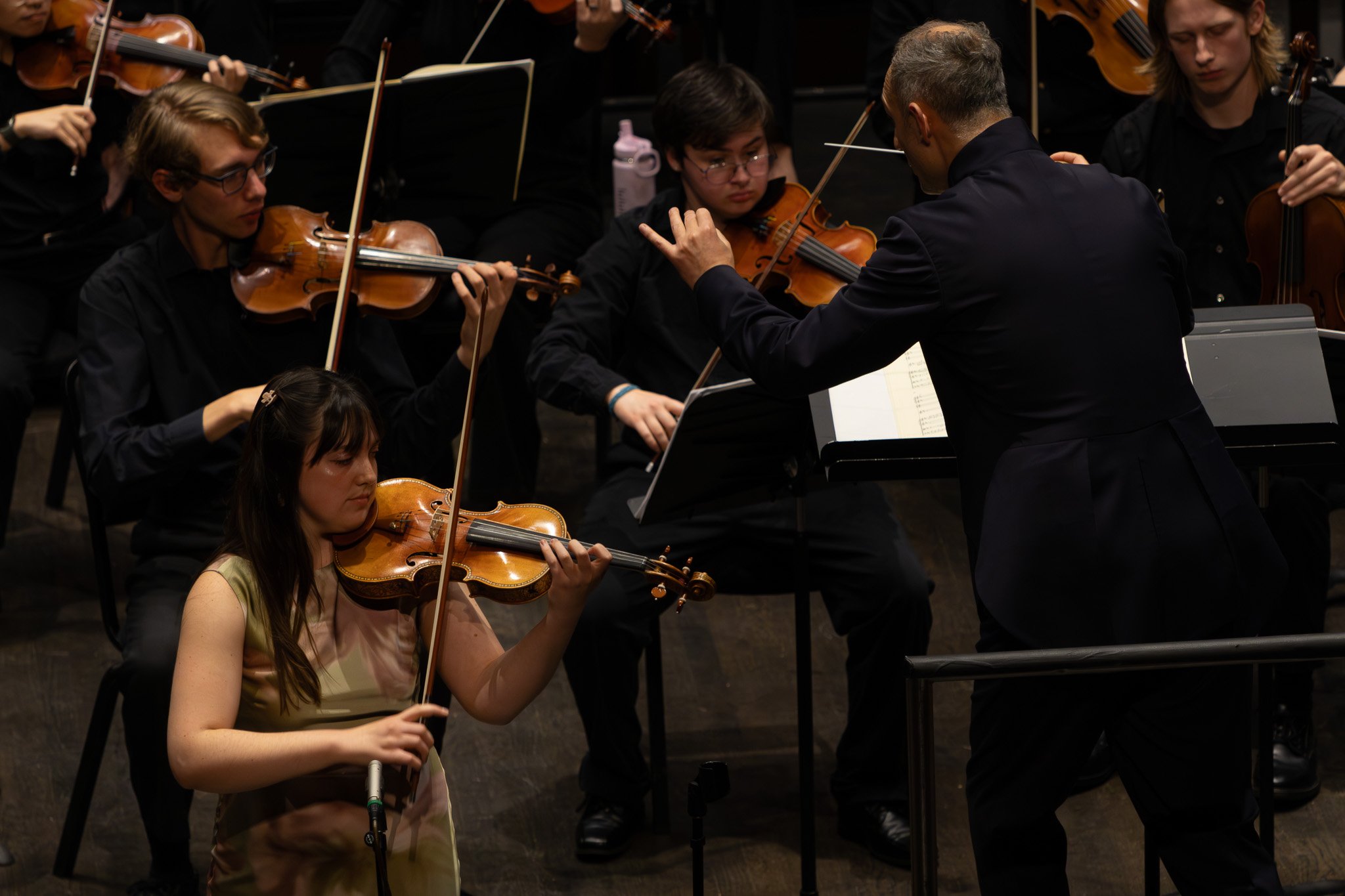 Orchestra conductor leading young musicians playing violins during a performance.