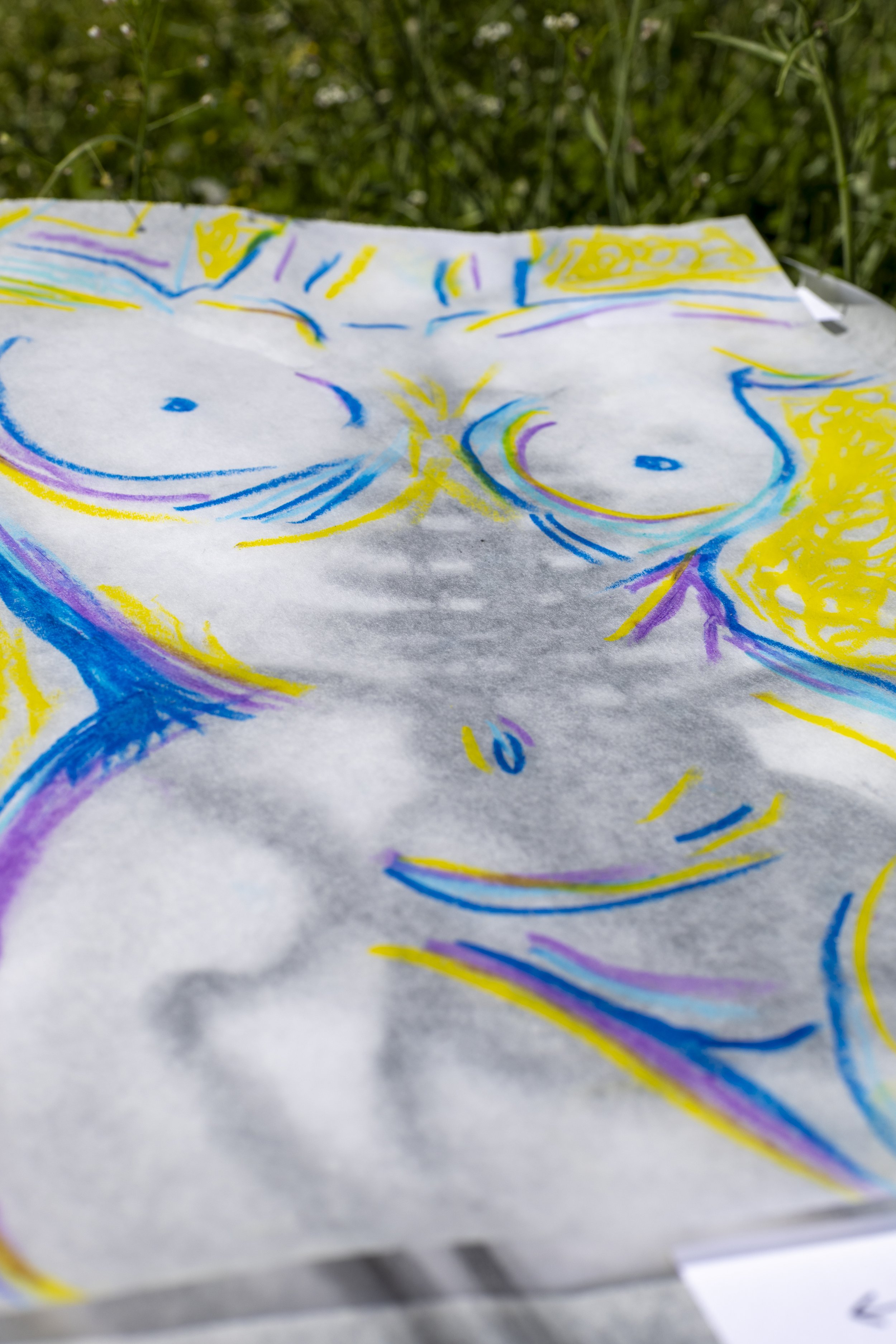 Colorful hand-drawn illustration of a woman's face on a piece of paper outdoors, with a background of grass.