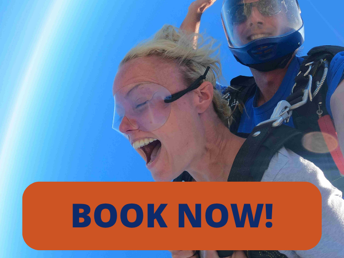 Tandem skydiving passenger laughing mid-jump with her instructor, harnessed together against a blue sky.