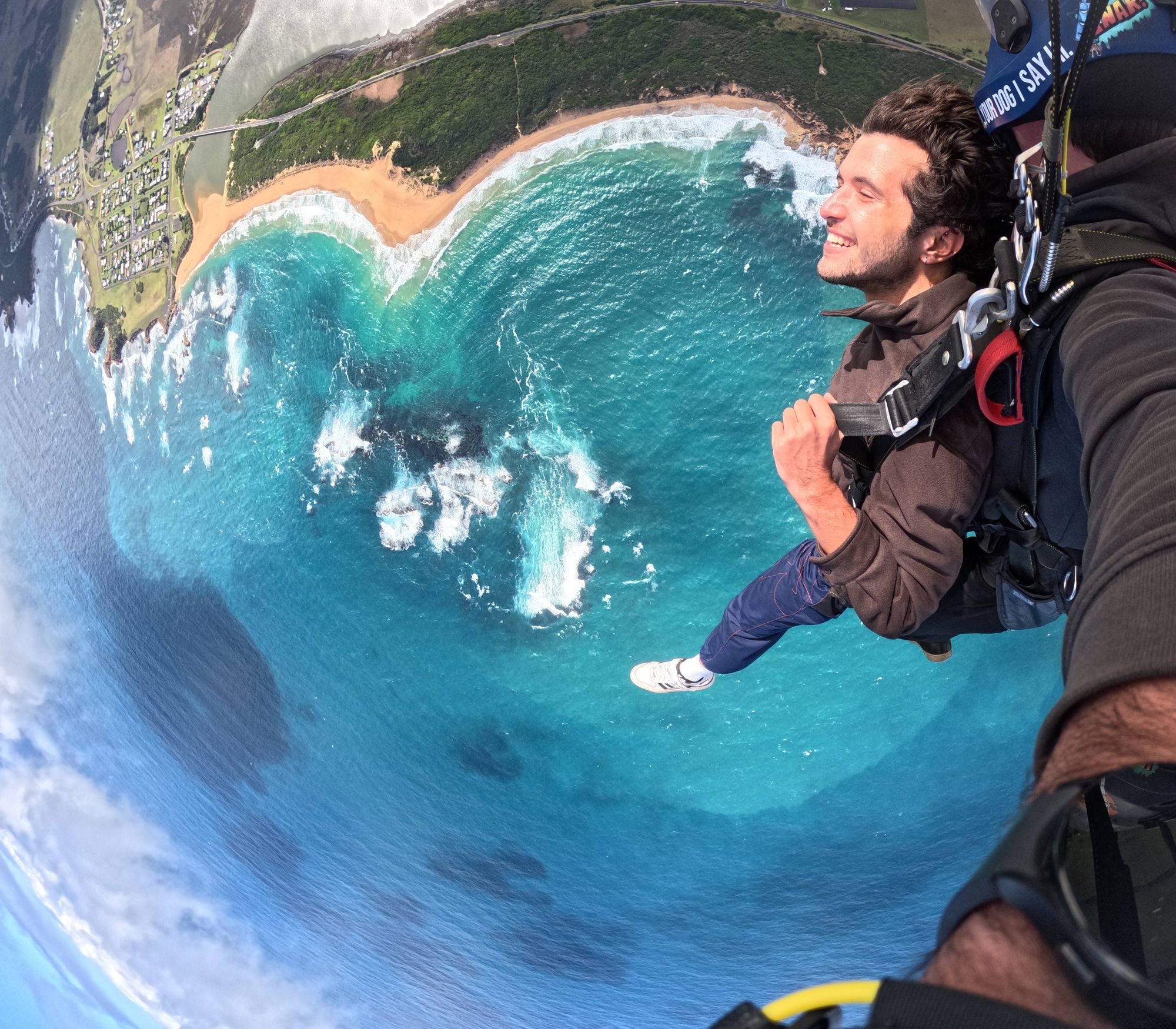 Tandem skydiver smiling in freefall above the bay at Peterborough on the Great Ocean Road