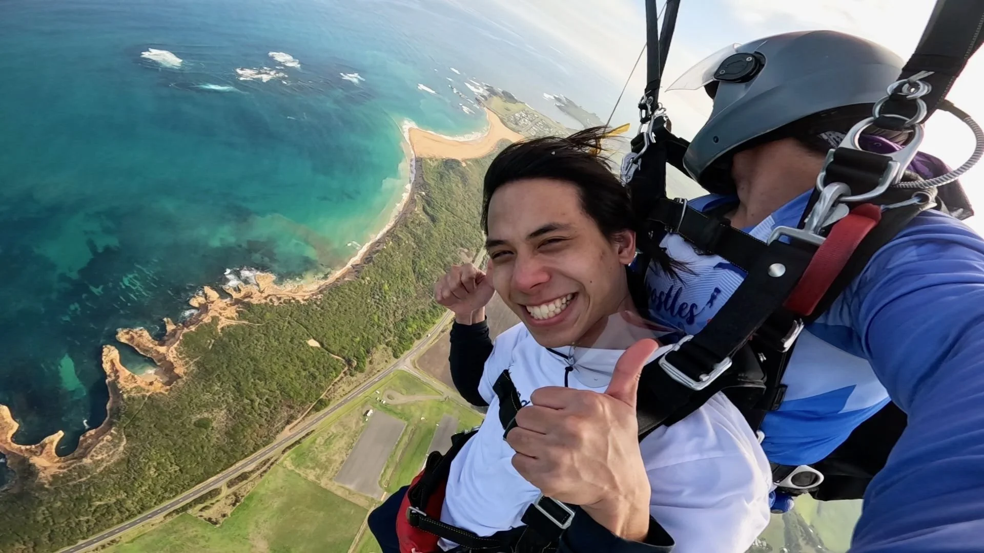 Happy tandem skydiver giving a thumbs up above the Great Ocean Road and airport