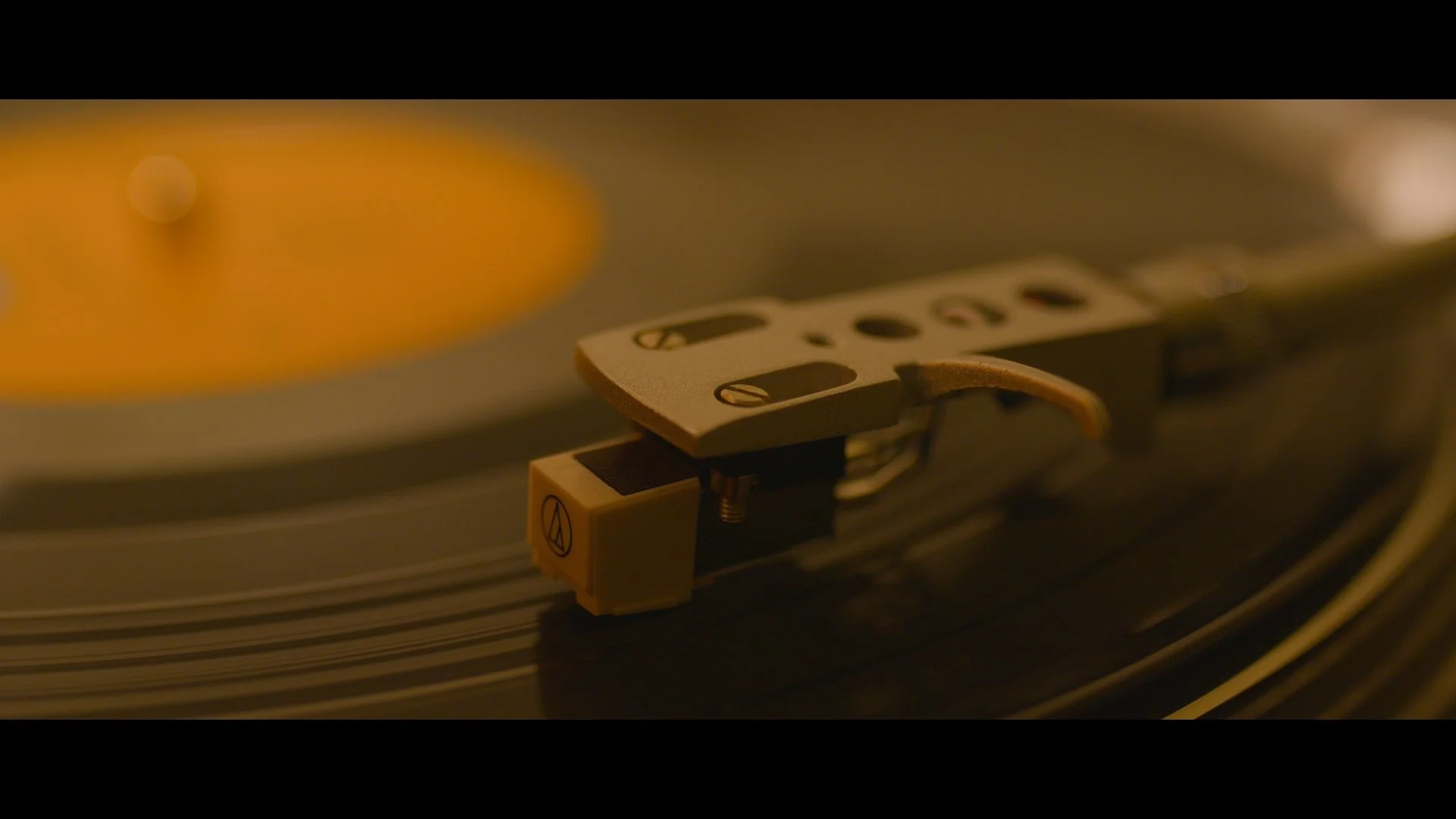 Close-up of a turntable's tonearm and stylus tracing a record's grooves in dim, warm lighting.