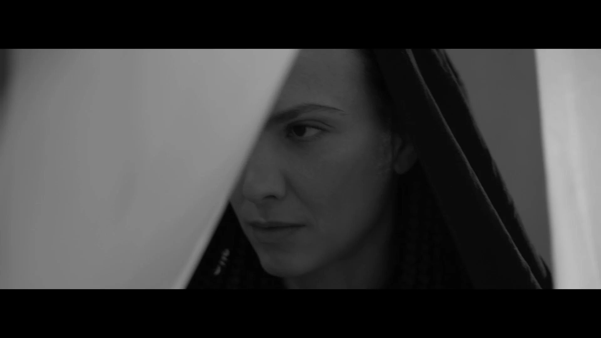Close-up of a woman's face partially hidden behind a diagonal plane, with intense eye expression, black hoodie, and black and white tone.