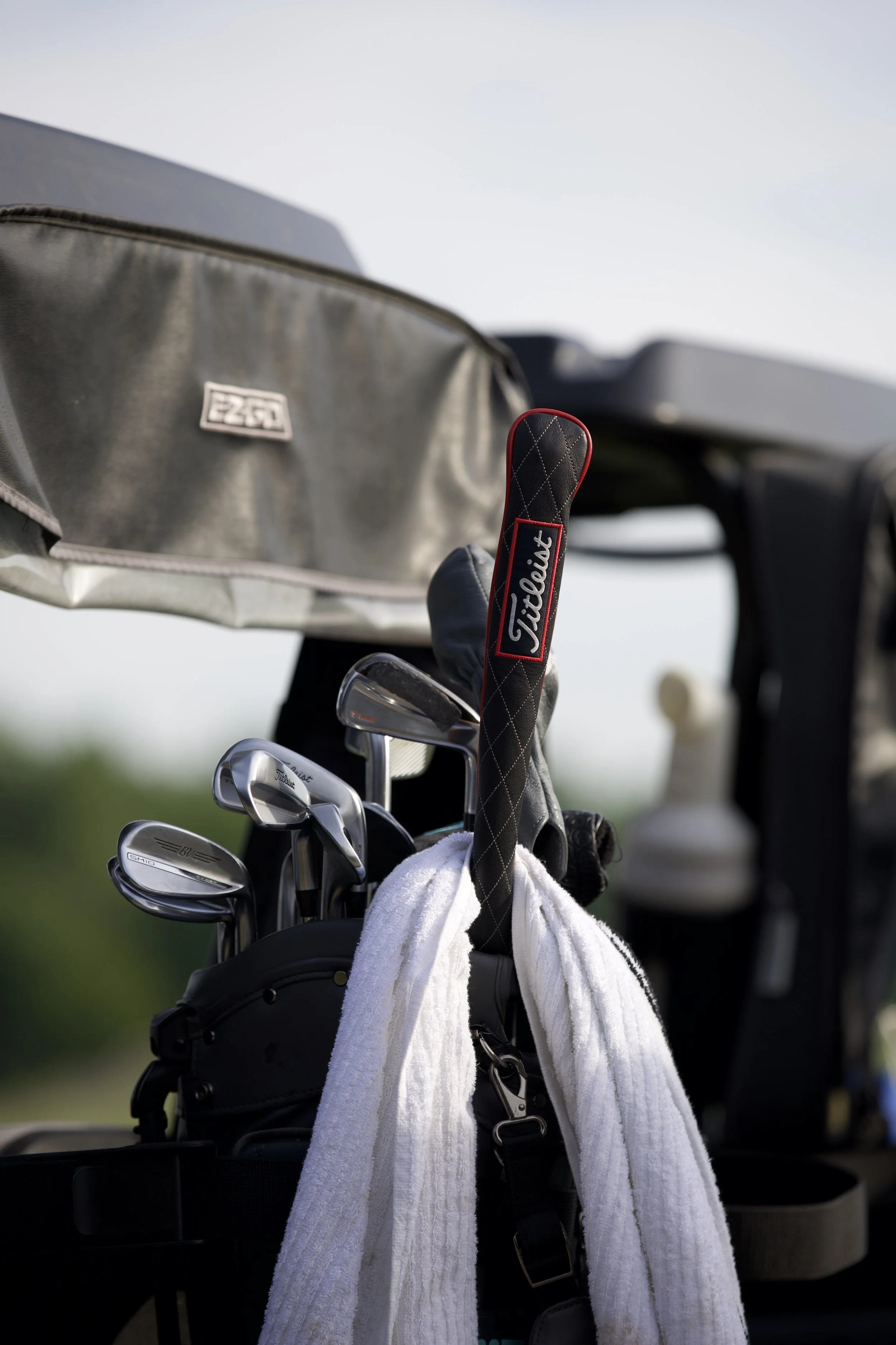 Golf bag with clubs, a white towel, and a Titleist towel attached, on a cart at a golf course.