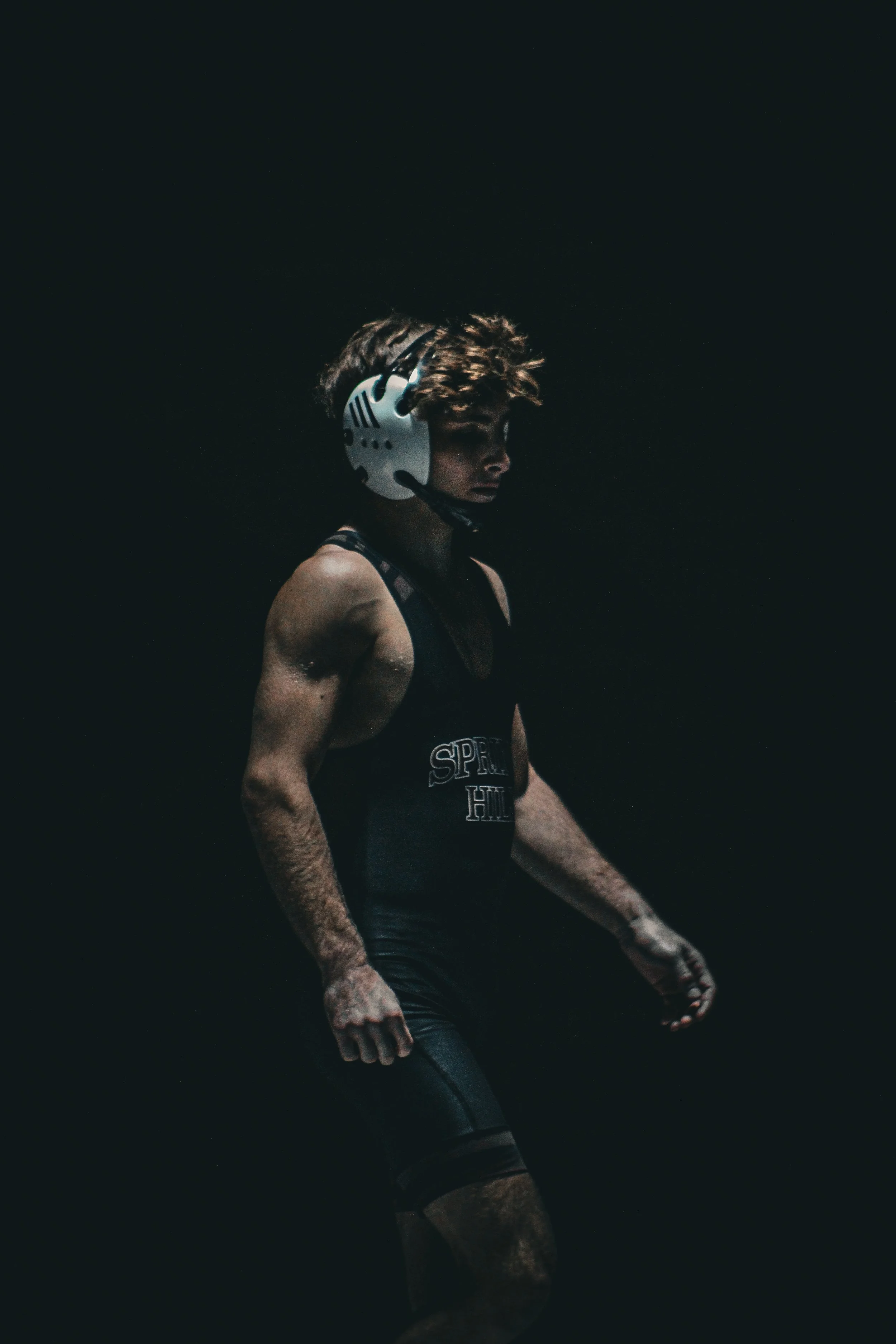 A person wearing a white helmet and black athletic clothing stands in a dark background with a somber expression.