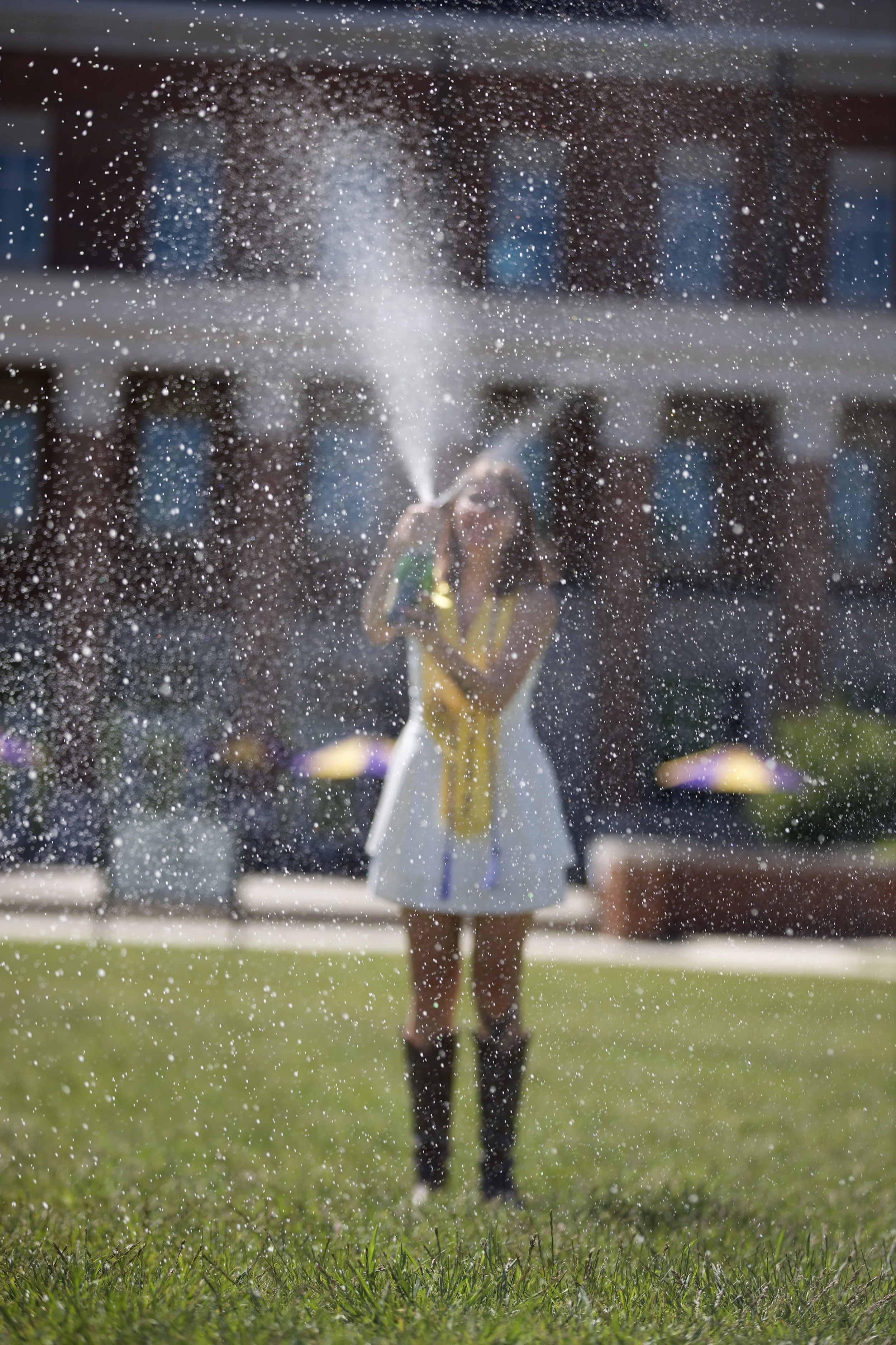 A girl running through sprinklers on a grassy field, with water spraying around her.