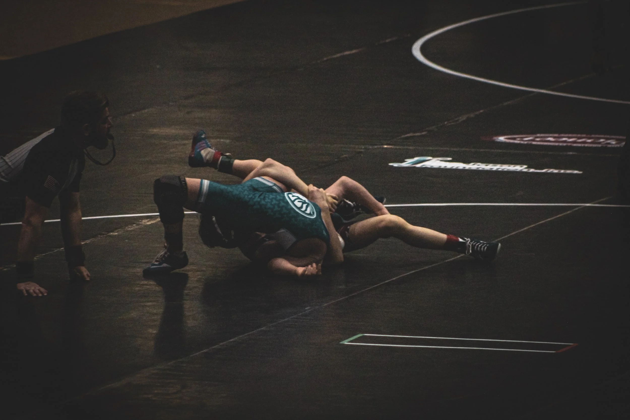 Wrestlers on the mat during a match with a referee observing.