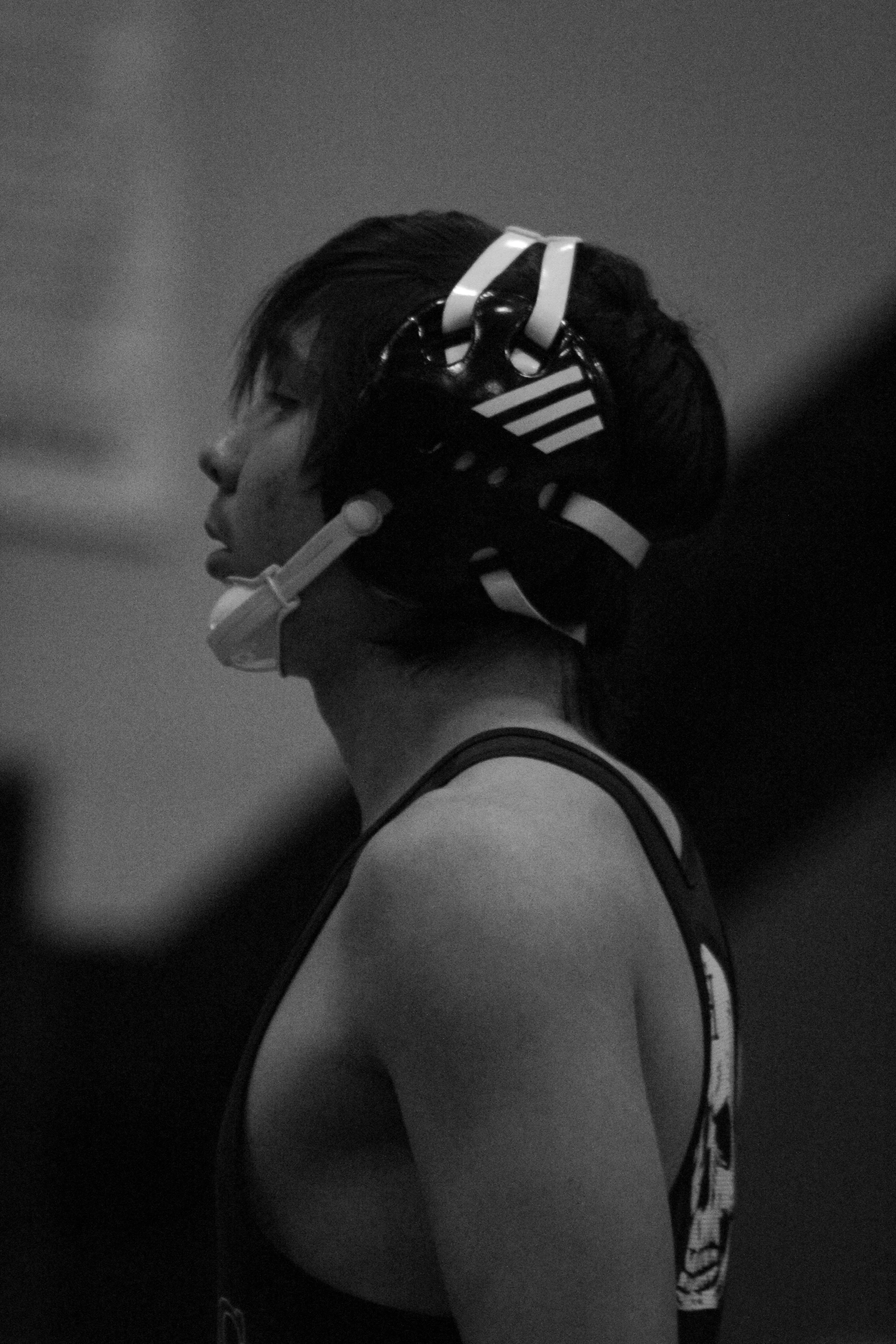Side profile of a person wearing a bike helmet, sporting a tank top, with a zebra pattern strap, and dark background.