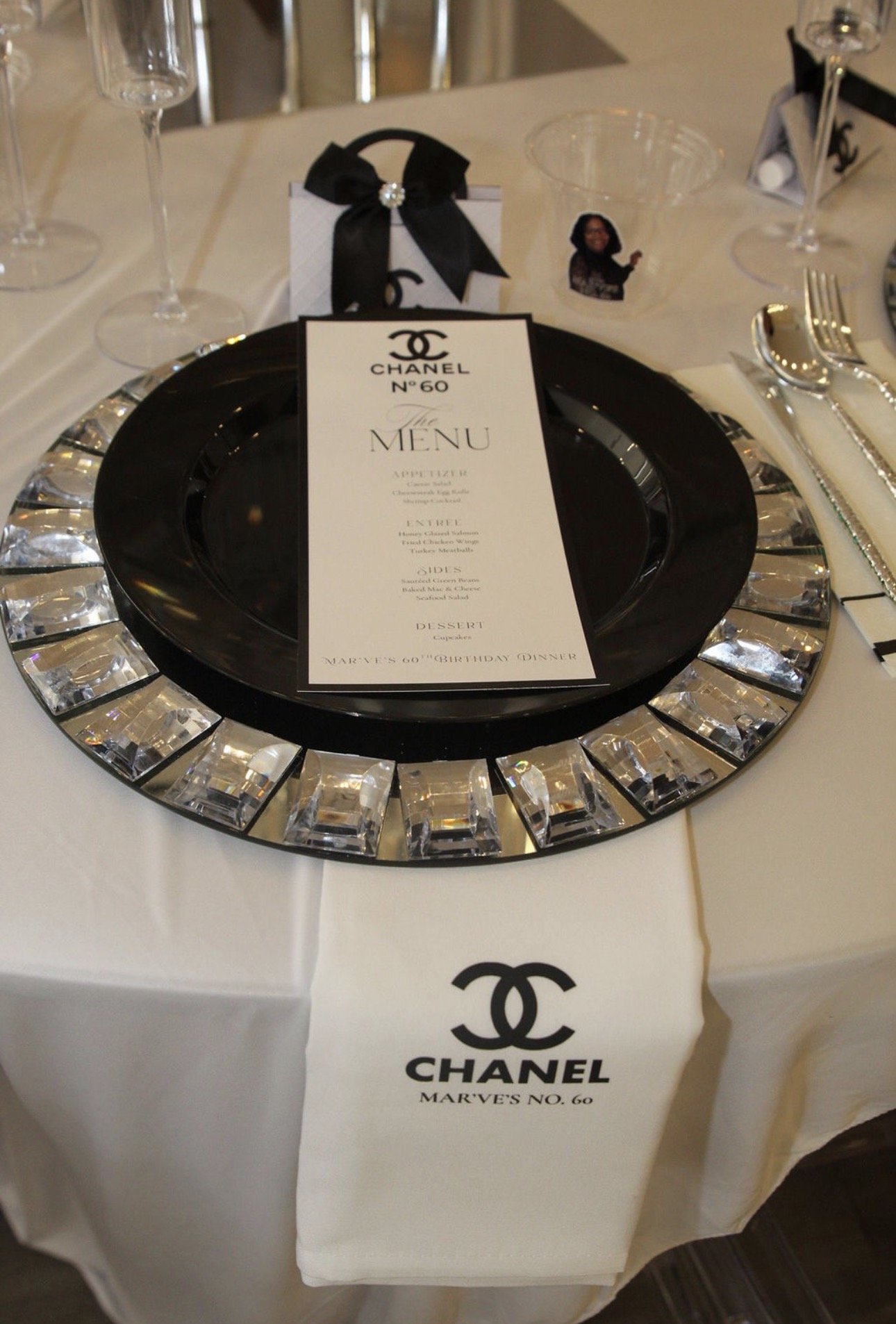 A decorated table with Chanel-themed decorations, including a menu, glasses, and a napkin with the Chanel logo. The table setup appears to be for a celebration, possibly a birthday party.Philadelphia event planner, Philadelphia birthday planner. Phil