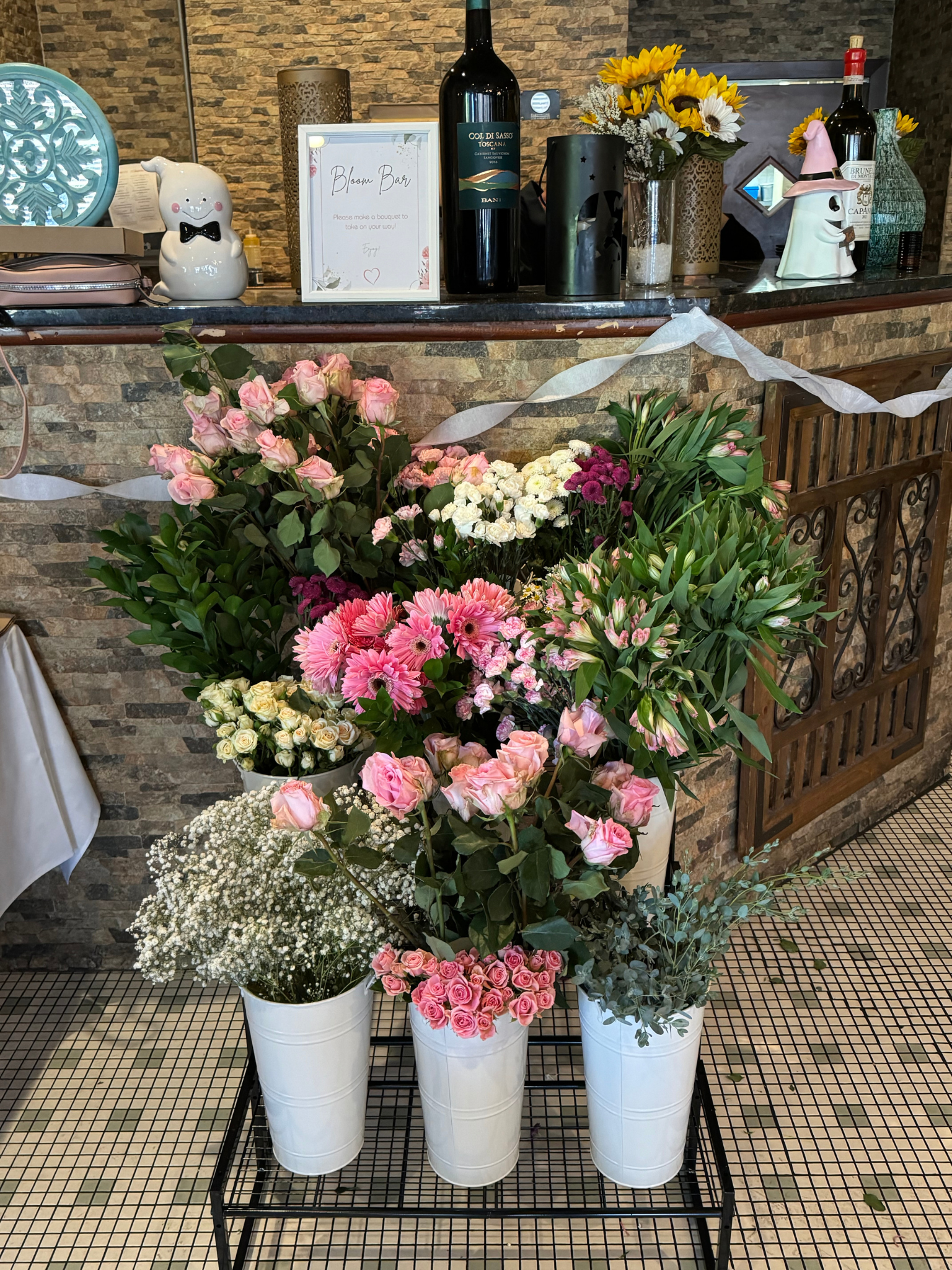 Various flower arrangements in white pots on a black stand in front of a brick wall, with additional flowers and decor on a shelf above.Philadelphia event planner, Philadelphia birthday planner. Philadelphia decorating, design, planning, and bridal