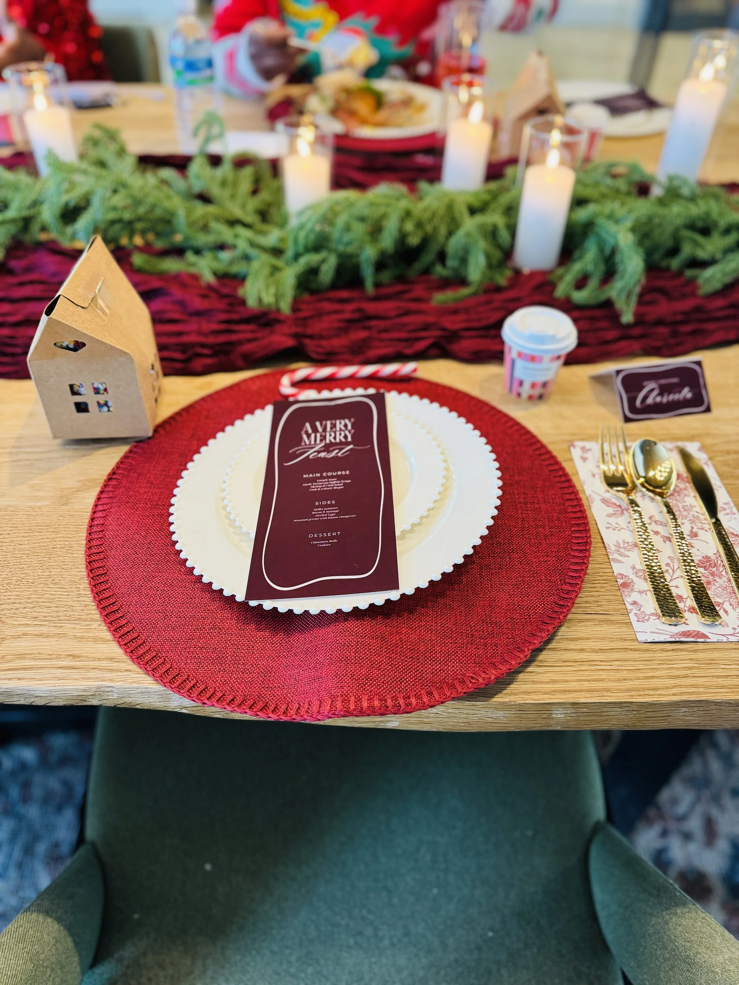 A holiday dining table with a red and white holiday-themed menu, a candy cane, silverware, candles, and greenery centerpiece, viewed from the person's perspective sitting at the tablePhiladelphia event planner, Philadelphia holiday planner