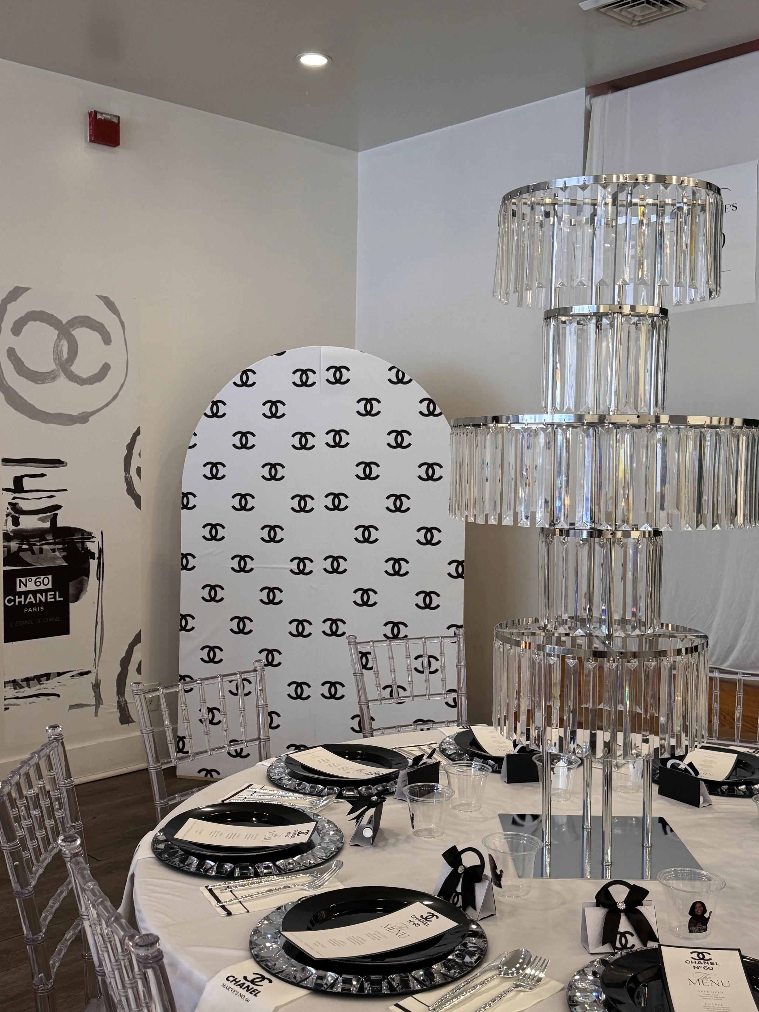 Elegant event table setup with black and silver Chanel-themed decorations, crystal chandelier, and black and white menus. Philadelphia event planner, Philadelphia birthday planner. Philadelphia decorating, design, planning, and event management