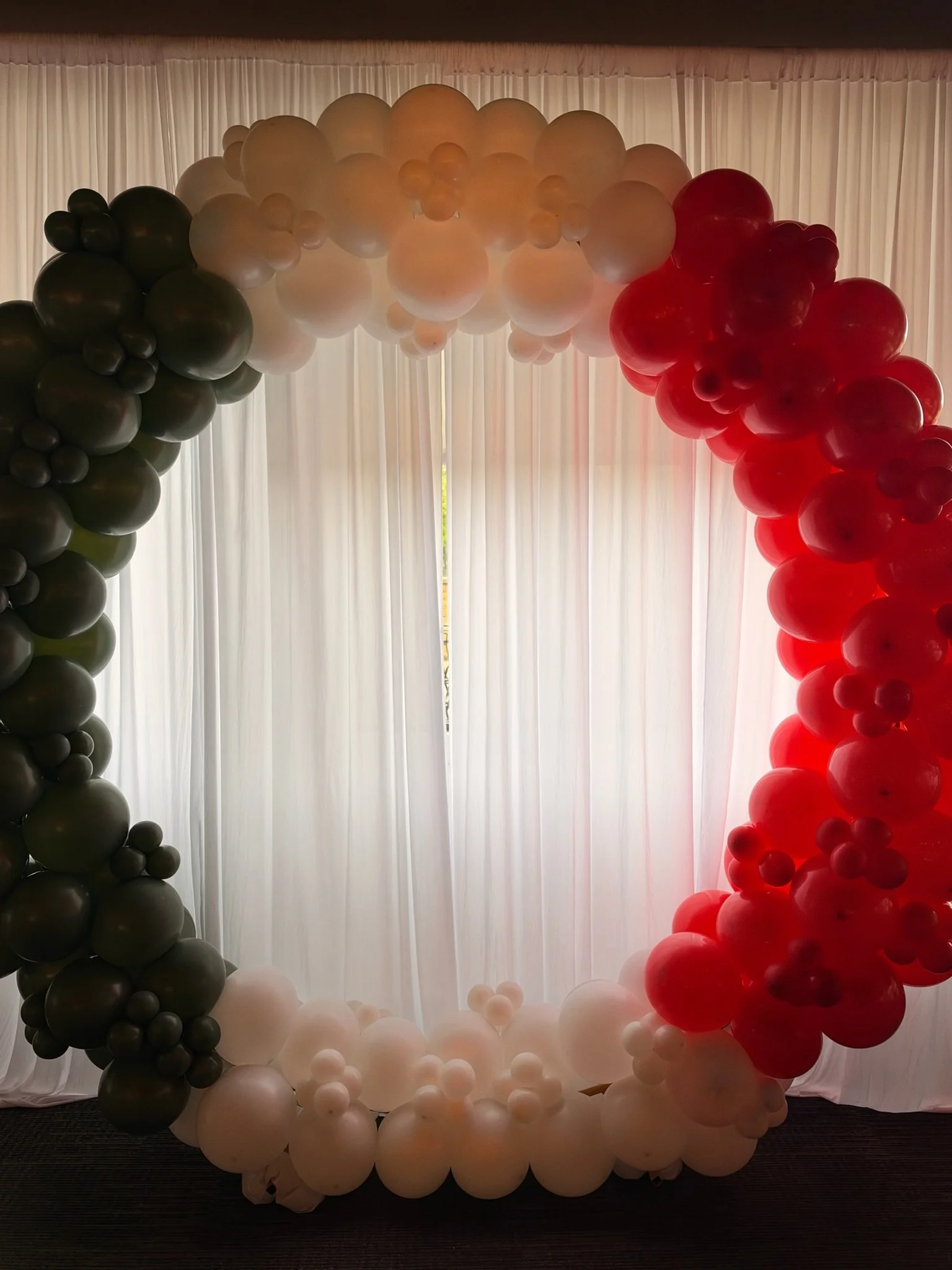 Balloon arch with black, white, and red balloons against a curtain backdrop.
