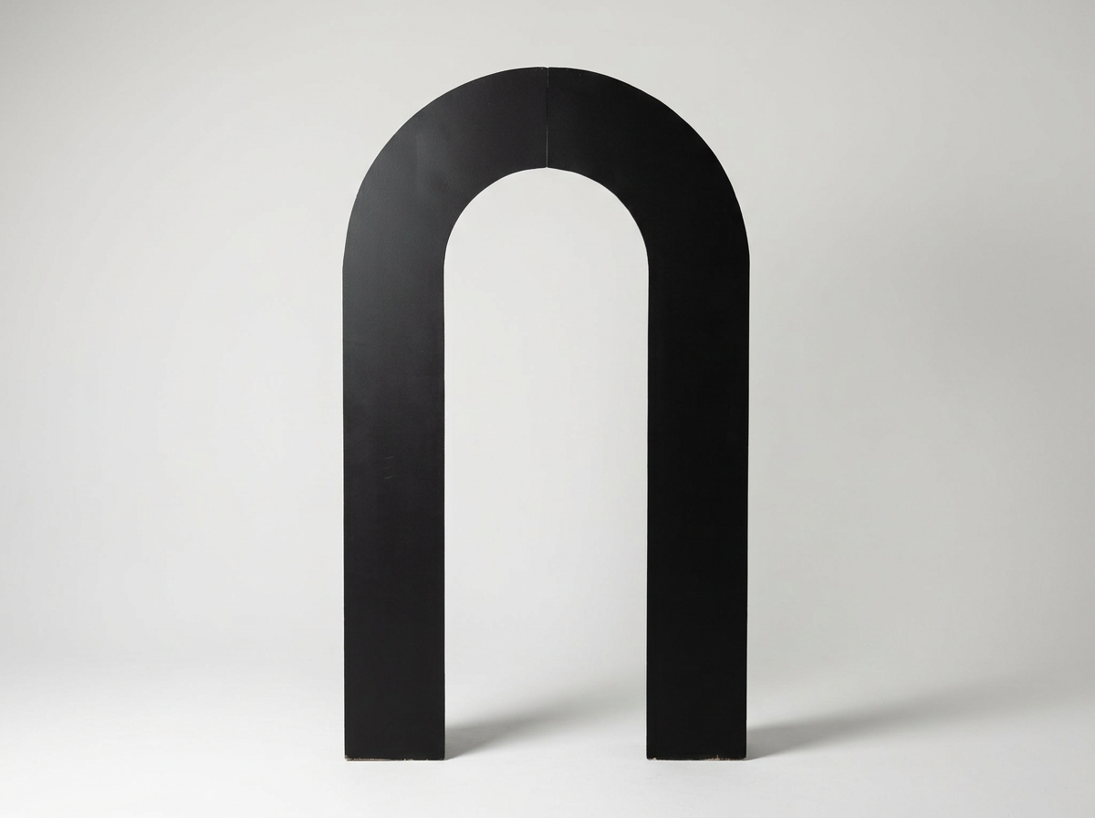 Large black horseshoe-shaped object standing upright on a plain, light-colored background.
