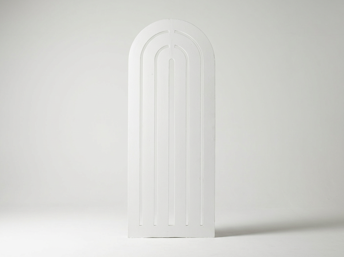 A white, minimalist, arched door with three vertical, slightly recessed grooves in a plain white room.